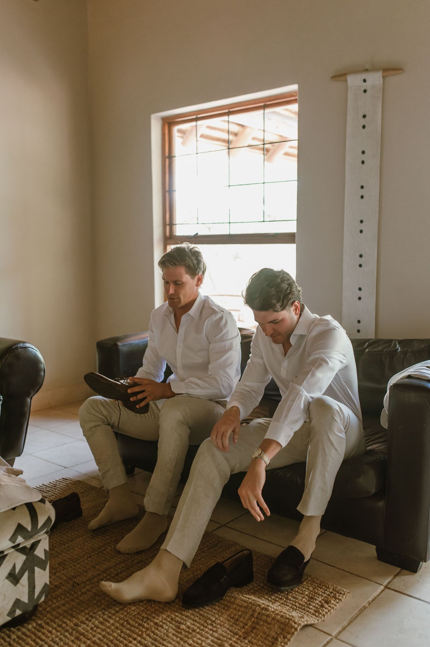 People in white suits sitting on brown leather couch in sunlit room.