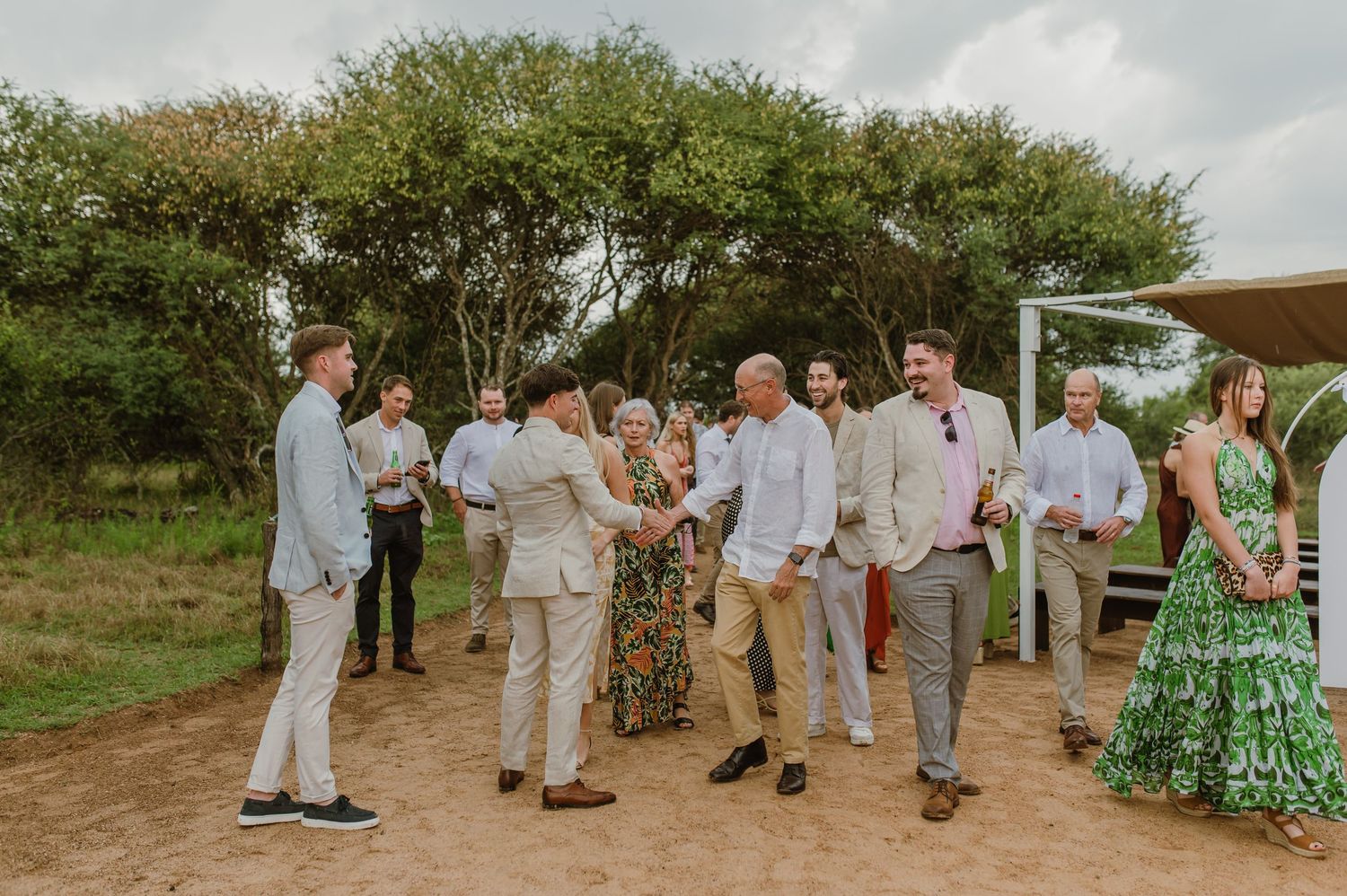 Guests mingling at an outdoor wedding ceremony with light-colored attire and natural surroundings.