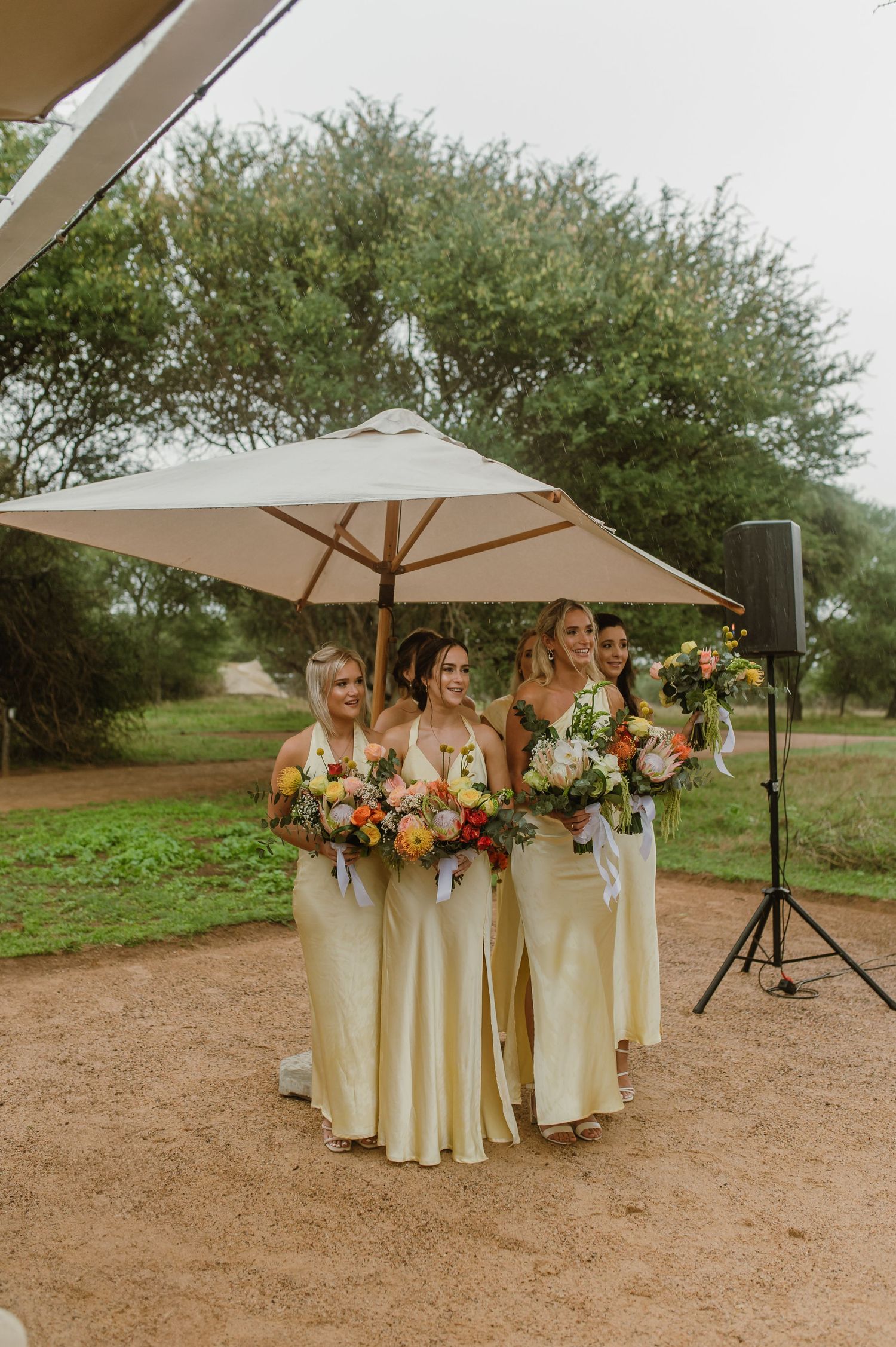 Bridesmaids in champagne dresses hold colorful bouquets at an outdoor wedding.