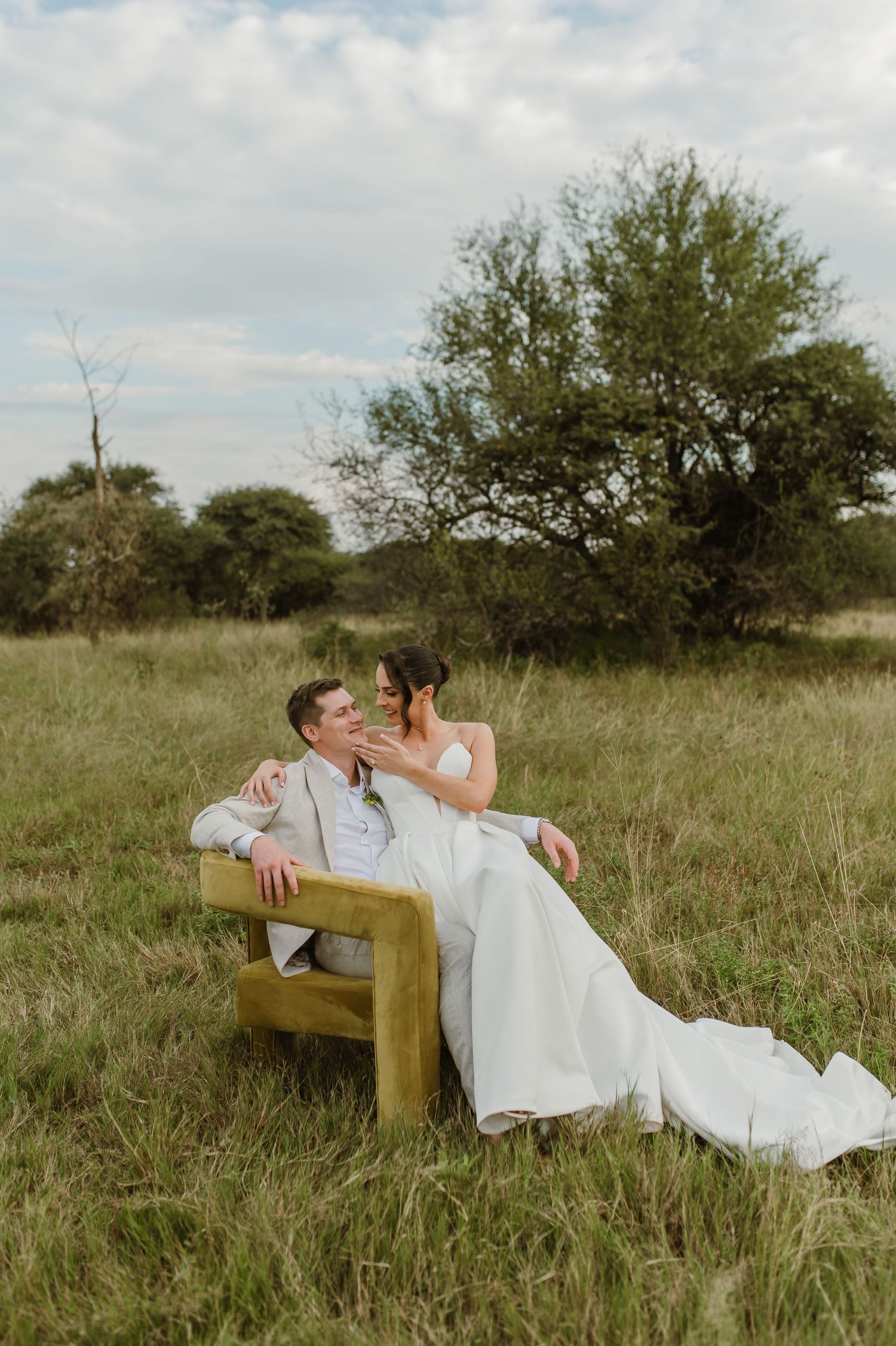 A couple lounges romantically on a wooden bench in a rustic field during golden hour.