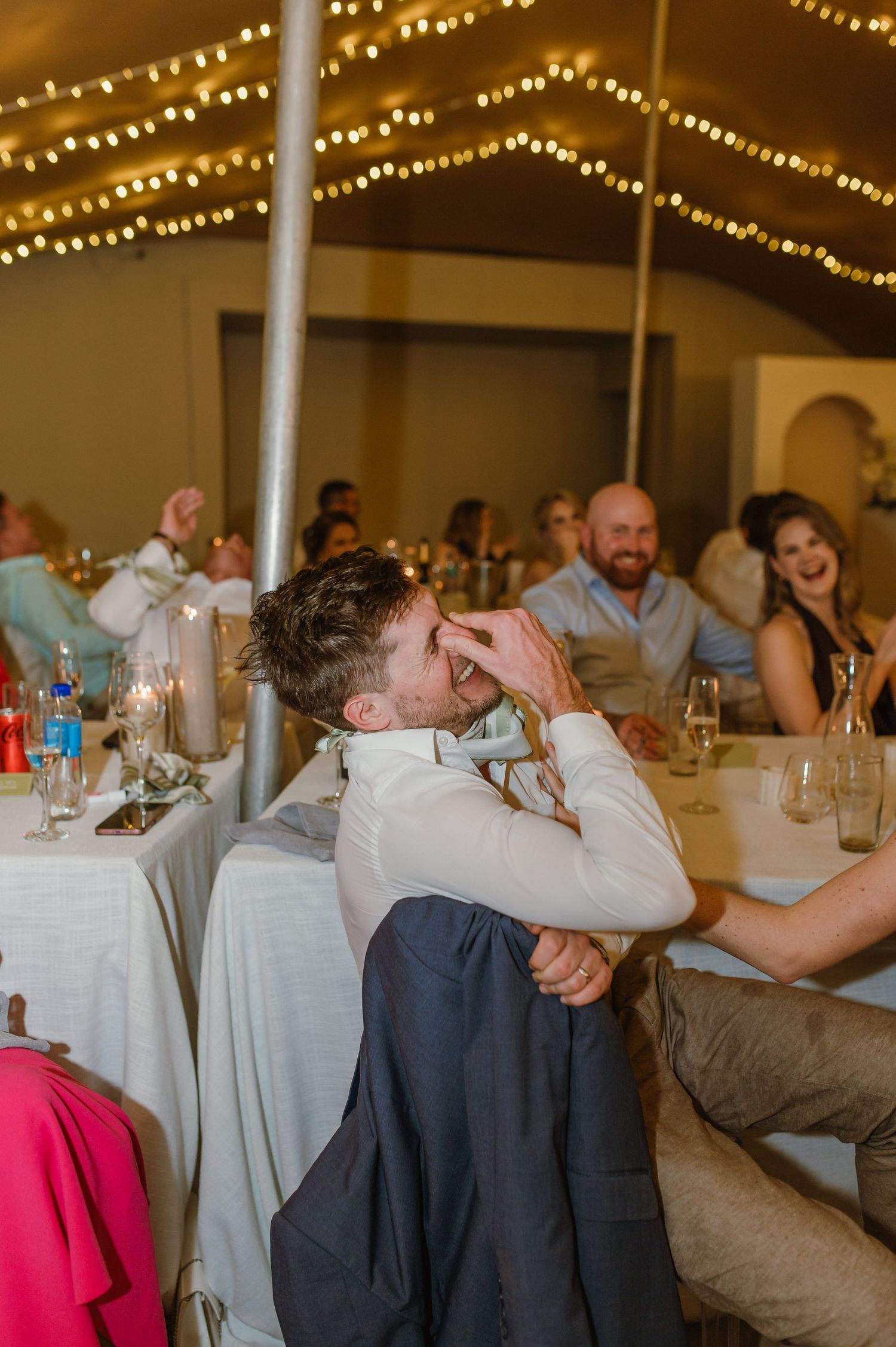 Wedding reception venue with string lights overhead and guests celebrating at round tables.