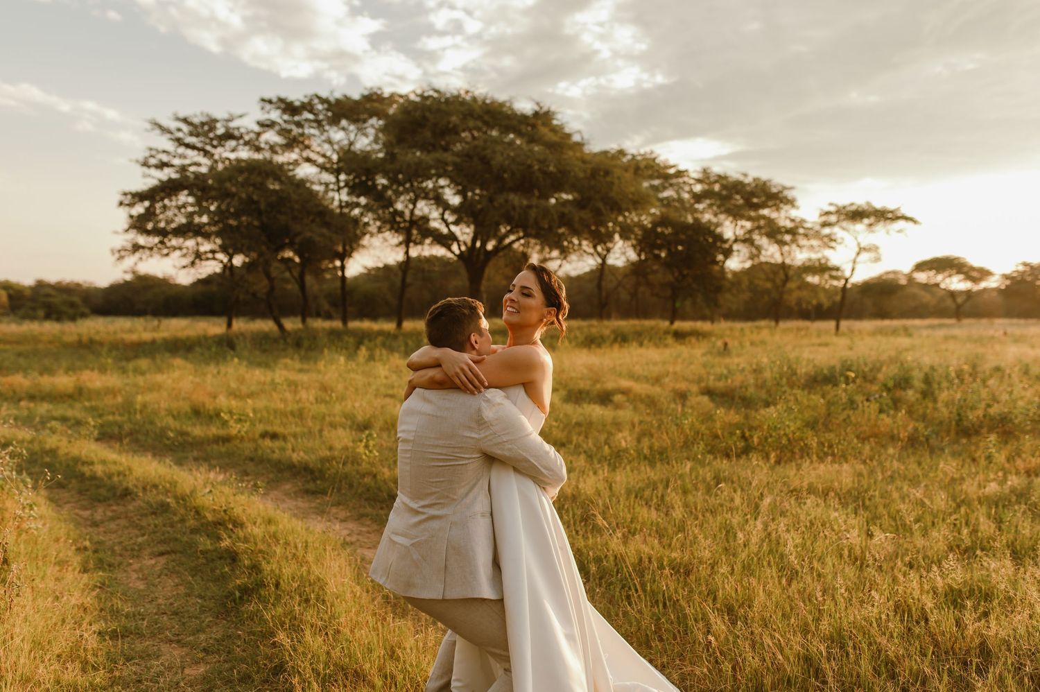 A wedding couple embraces while walking through a golden field at sunset.