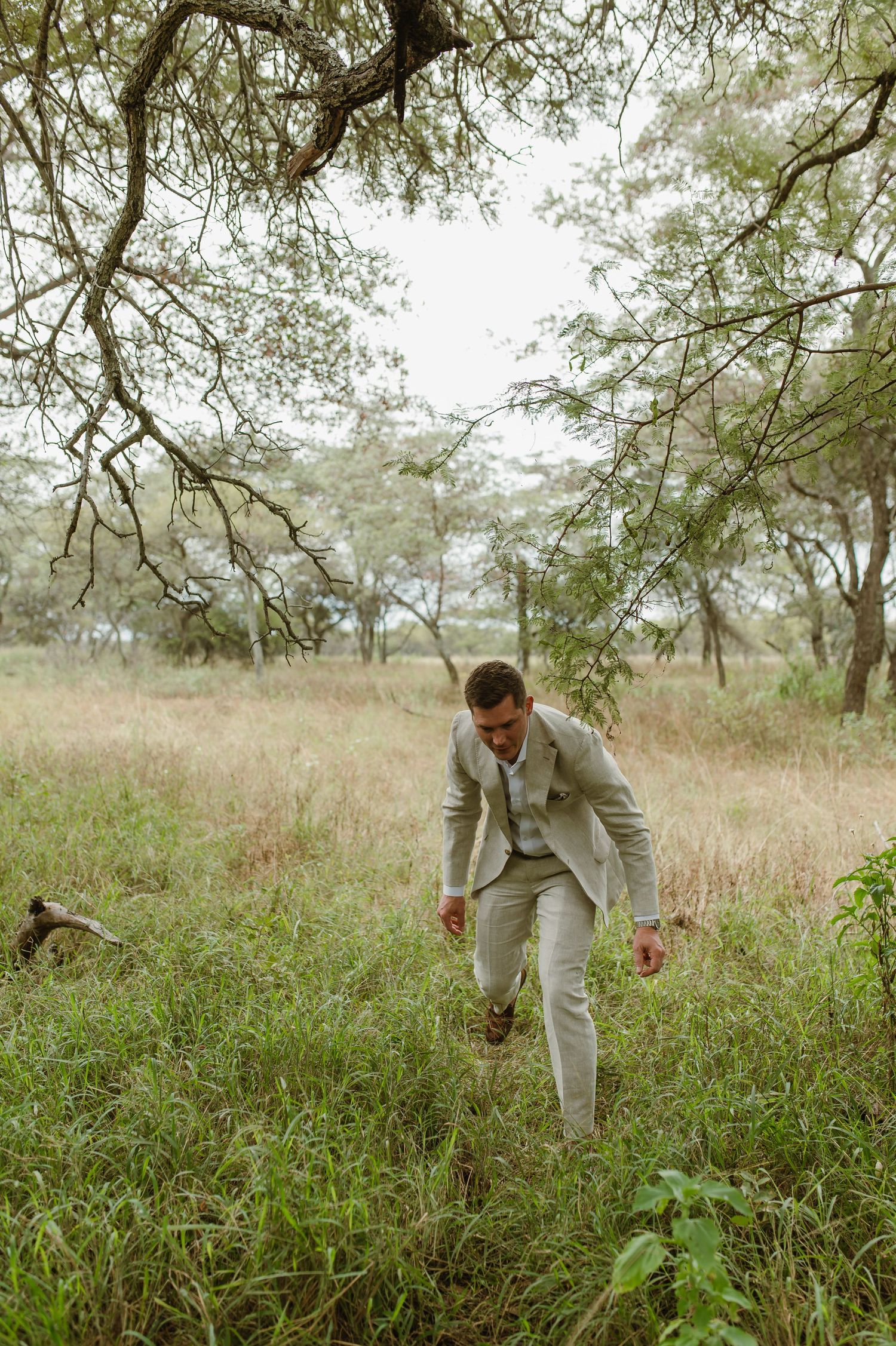 Person walking through tall grass in natural setting wearing light colored suit.