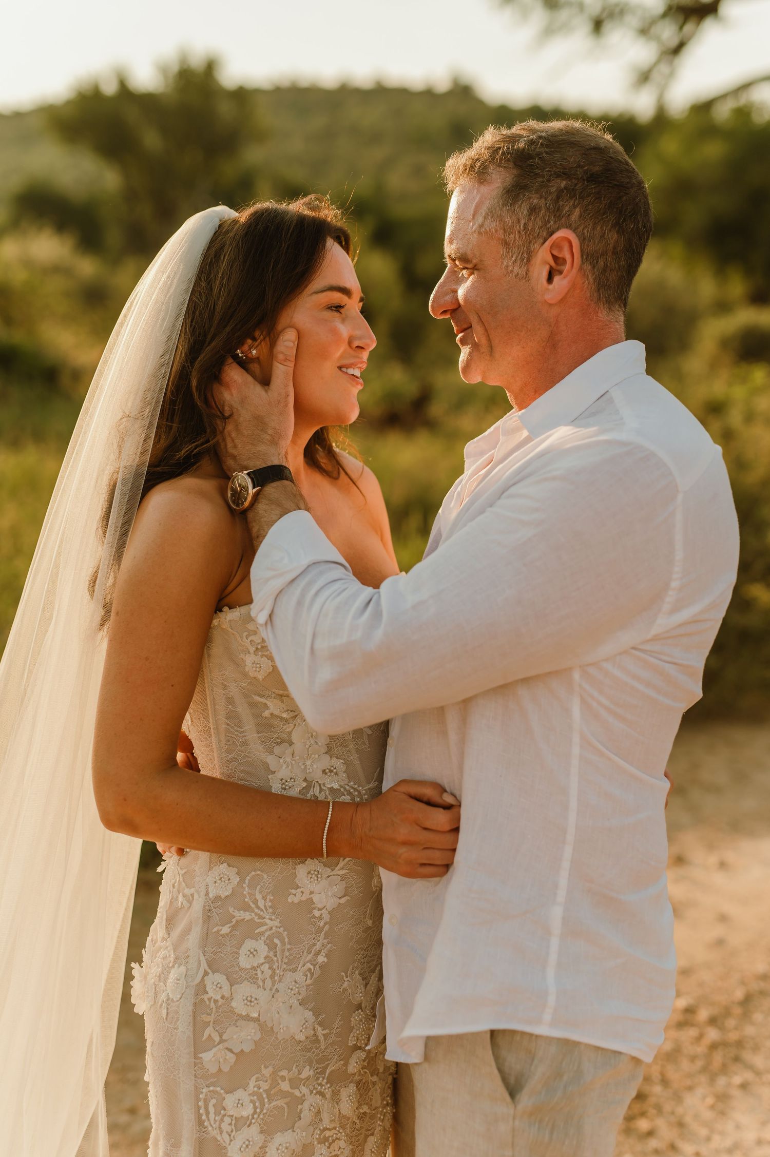 A smiling bride and groom share a tender moment at sunset in an outdoor wedding setting.