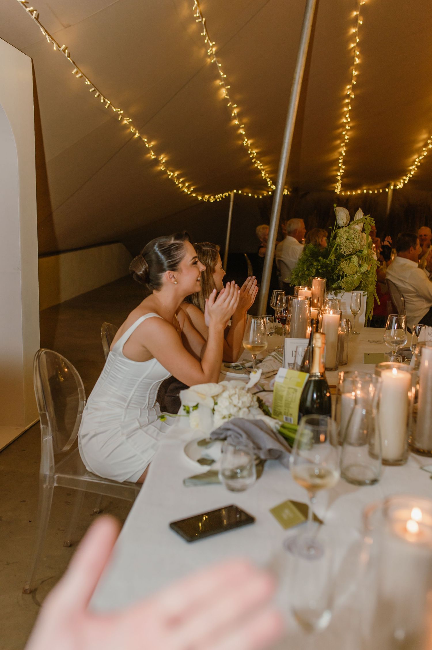Wedding reception table setting with candles and string lights creating warm ambiance.