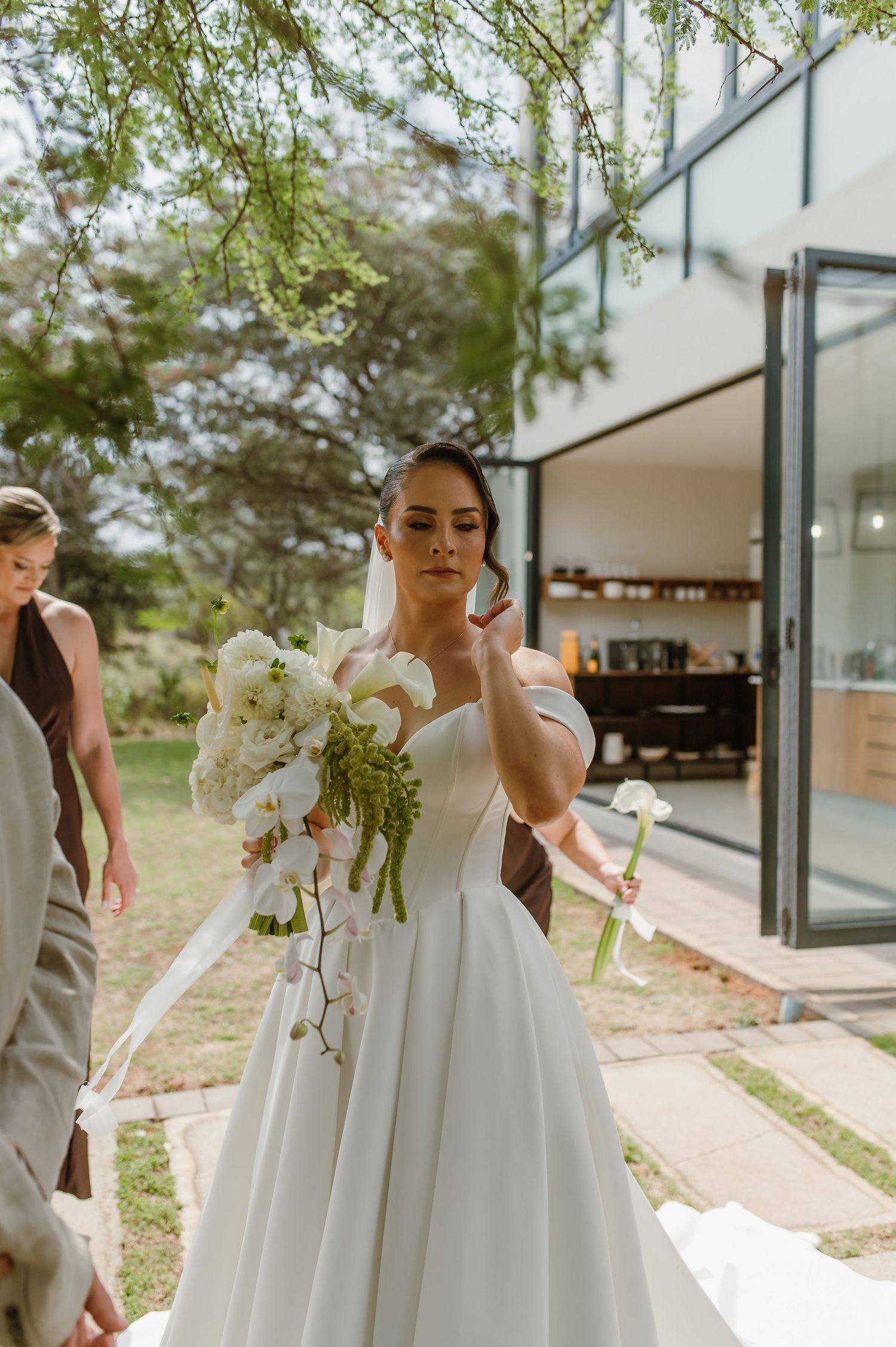 Elegant white wedding gowns and bouquets captured in a modern outdoor setting with glass architecture.