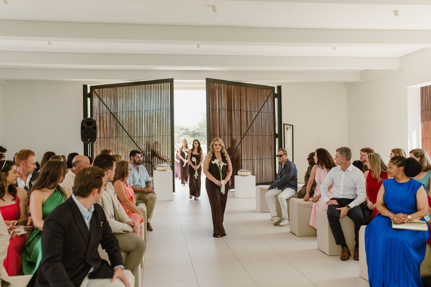 Wedding guests mingle in an elegant white modern interior space with high ceilings.