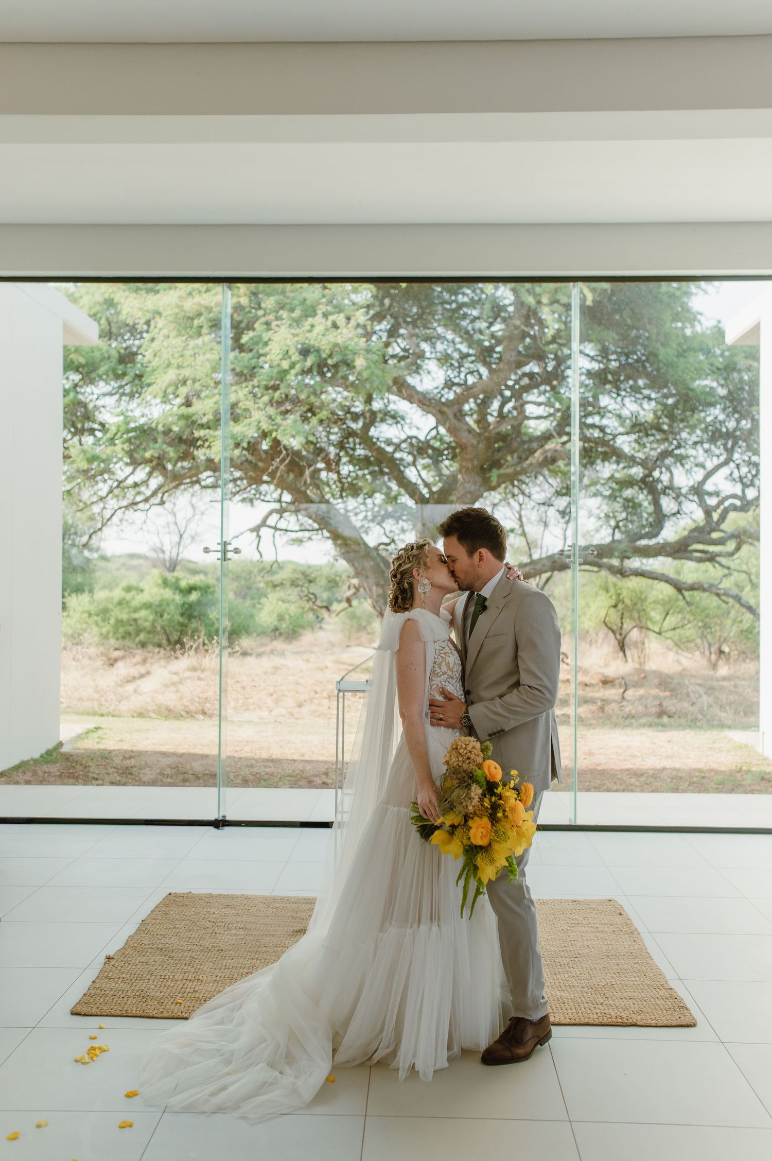 Couple shares intimate moment in modern venue with floor-to-ceiling windows overlooking nature.