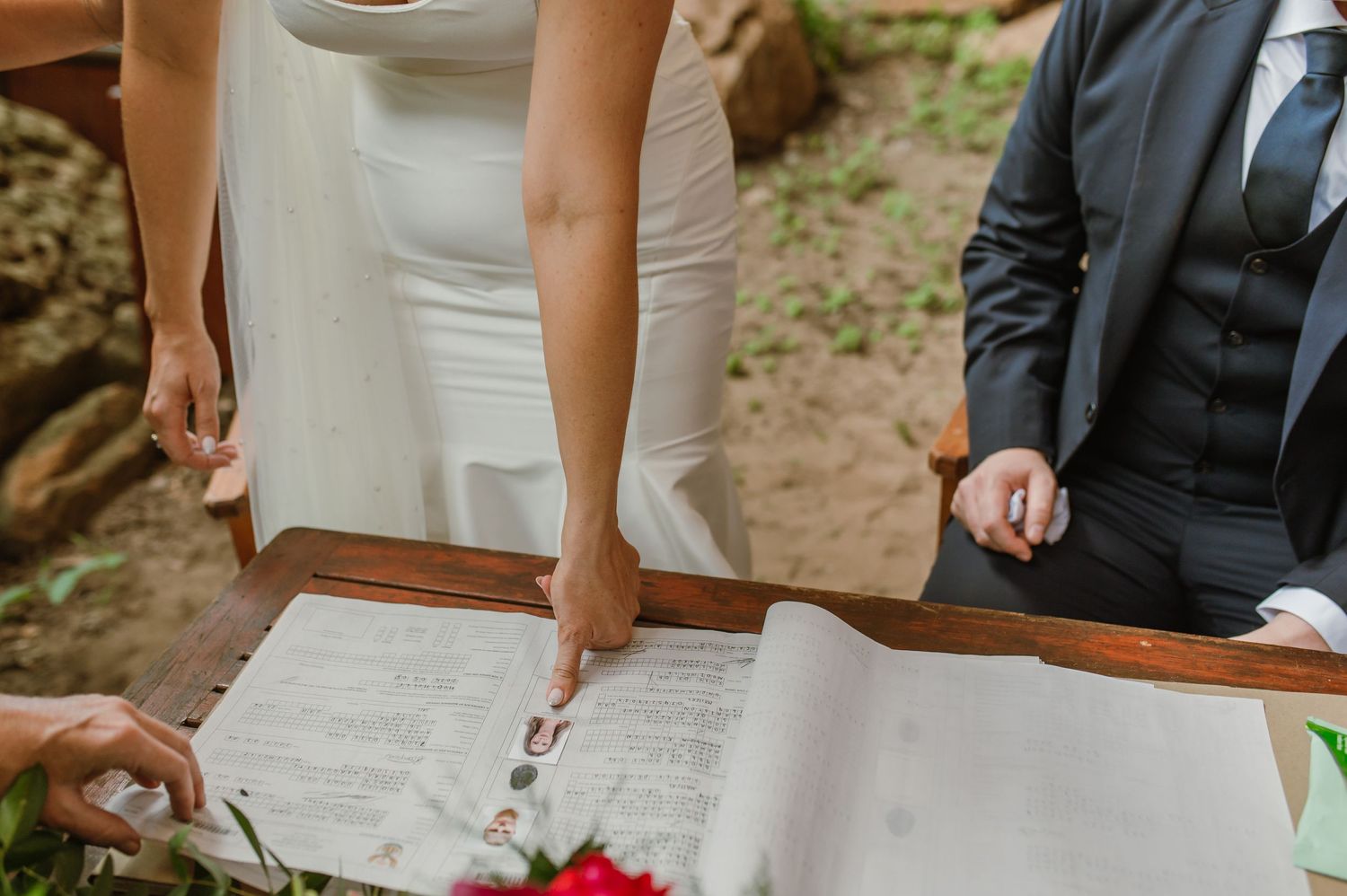 Close-up view of wedding ceremony document signing with wooden table in natural setting.