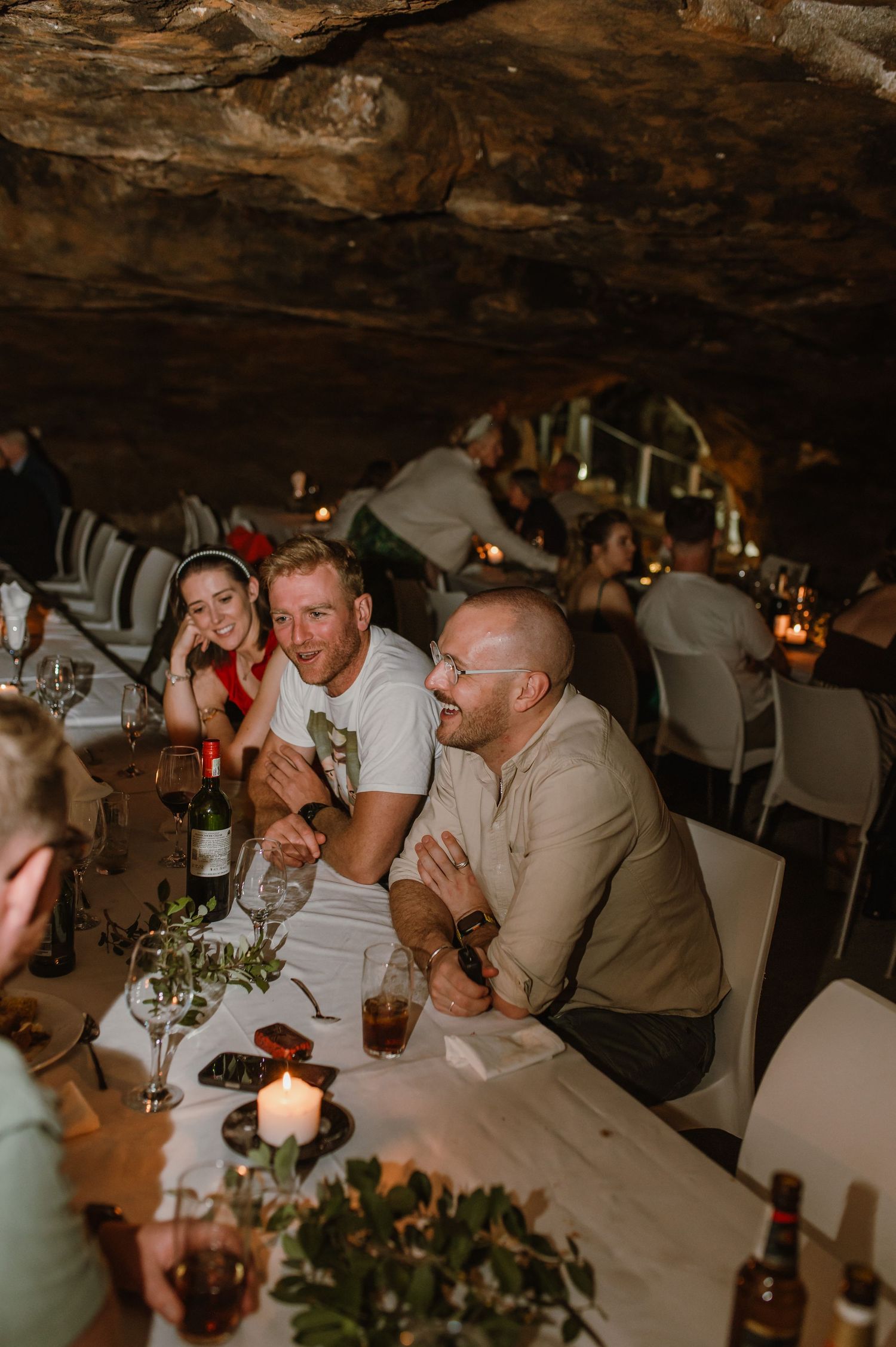Guests engaged in lively conversation at a cave dinner party with candlelit tables.