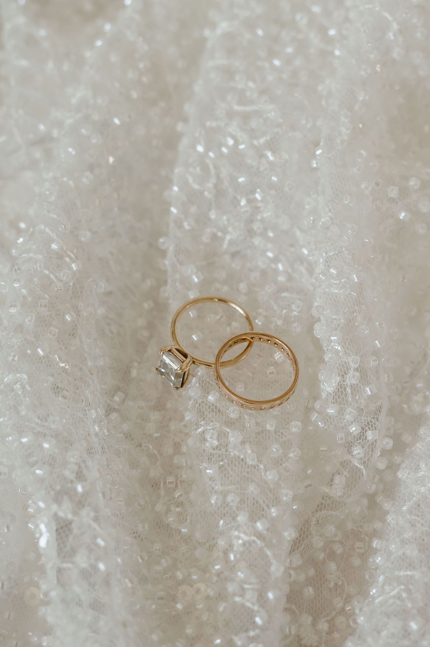 Gold wedding rings displayed on a sparkling white fabric background.