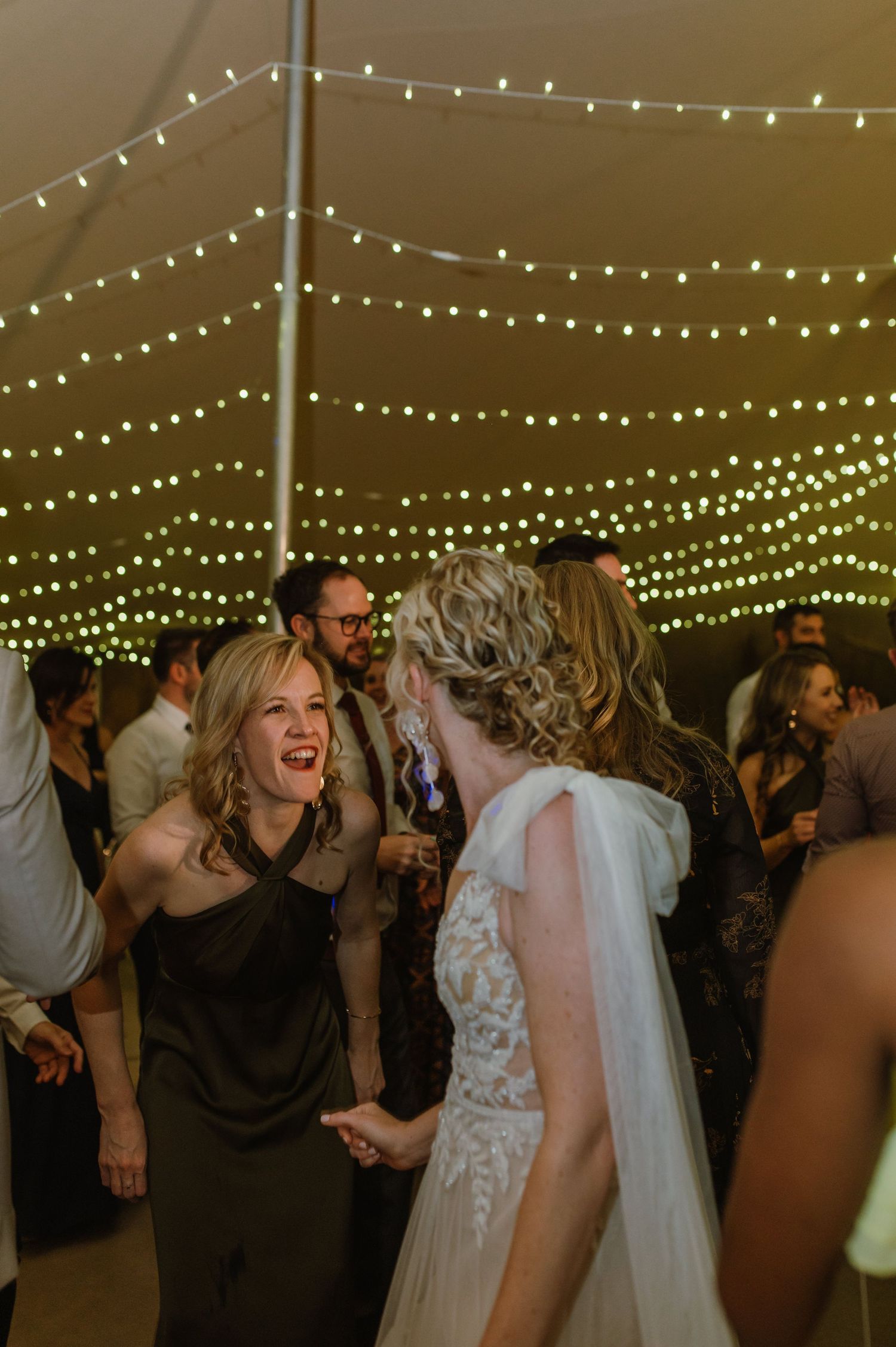Energetic dancing and celebration at wedding reception under twinkling lights.
