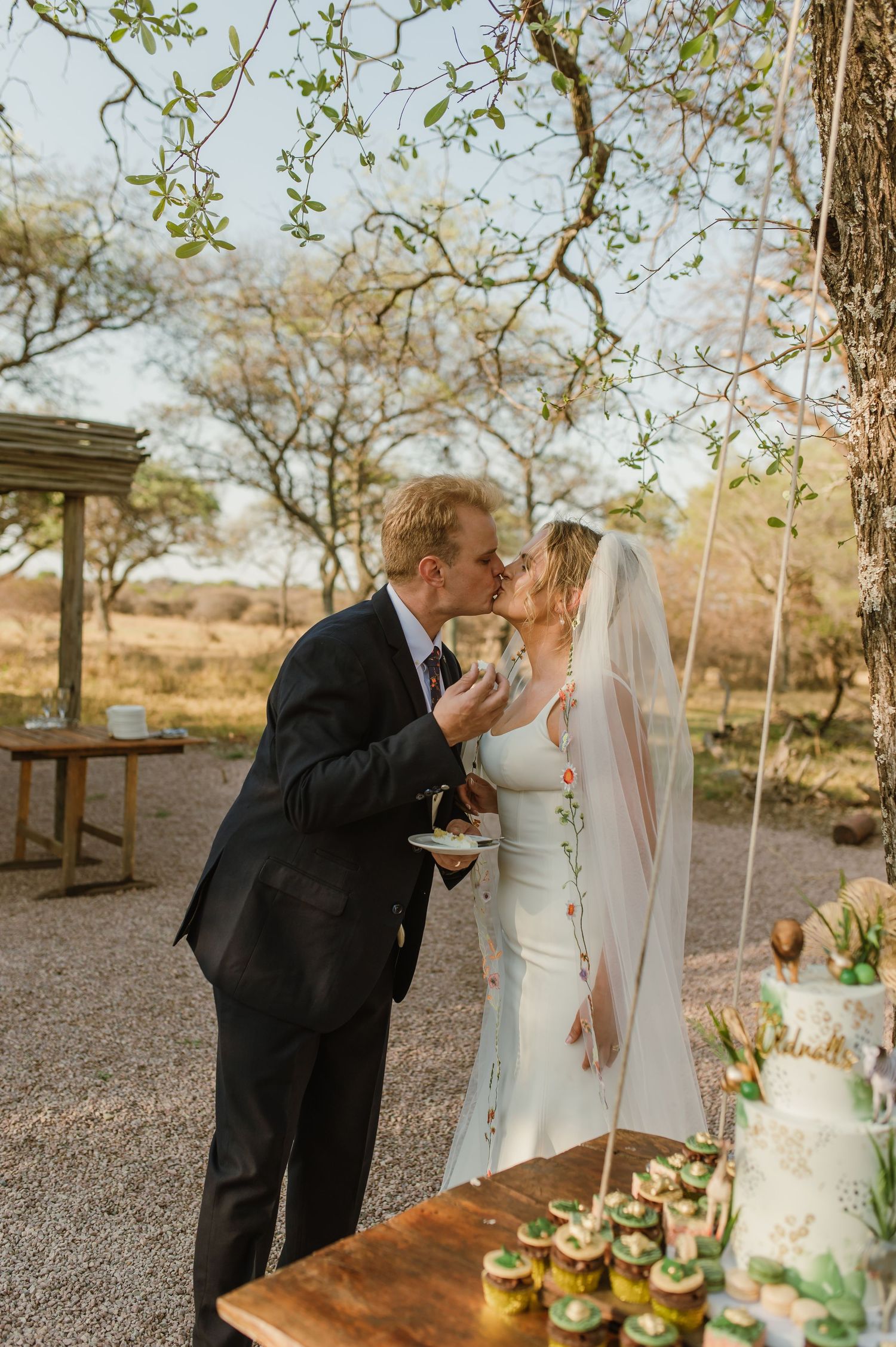 A wedding couple sharing food and laughter at a rustic outdoor table setting.
