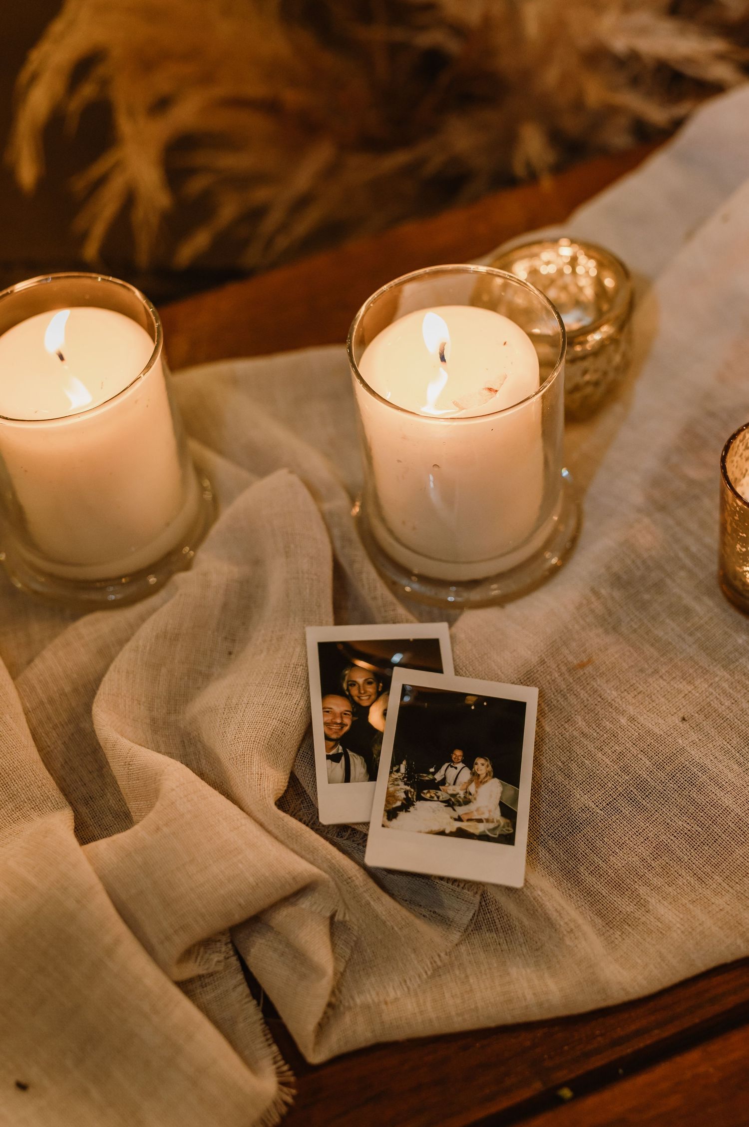 Wedding decor featuring white candles, linen fabric, and polaroid photos on a wooden surface.