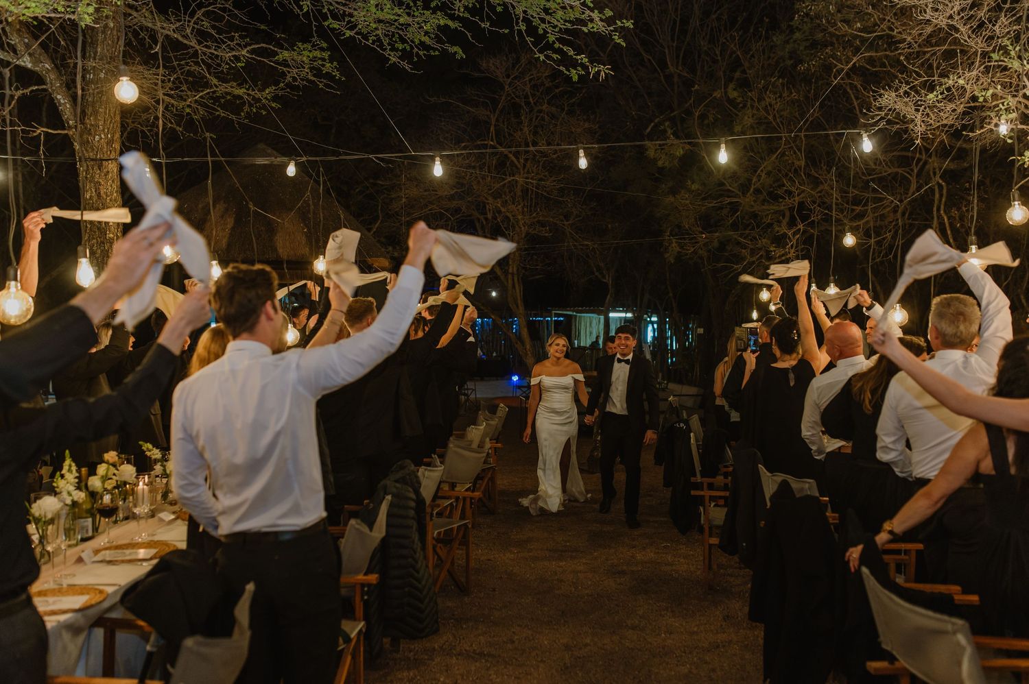 Wedding party dancing and celebrating under string lights at outdoor reception.