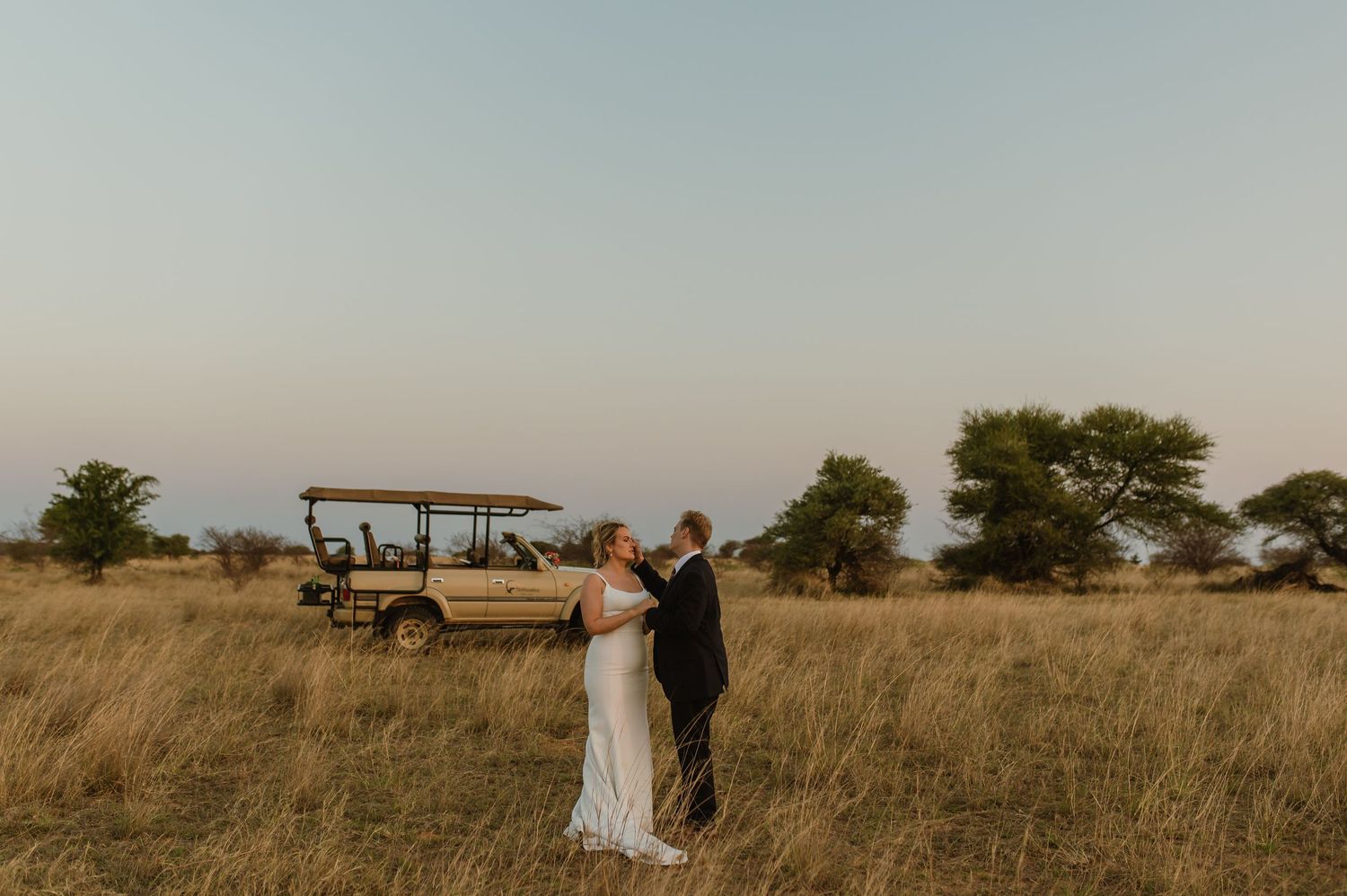 Wedding couple walking through savanna landscape at golden hour.