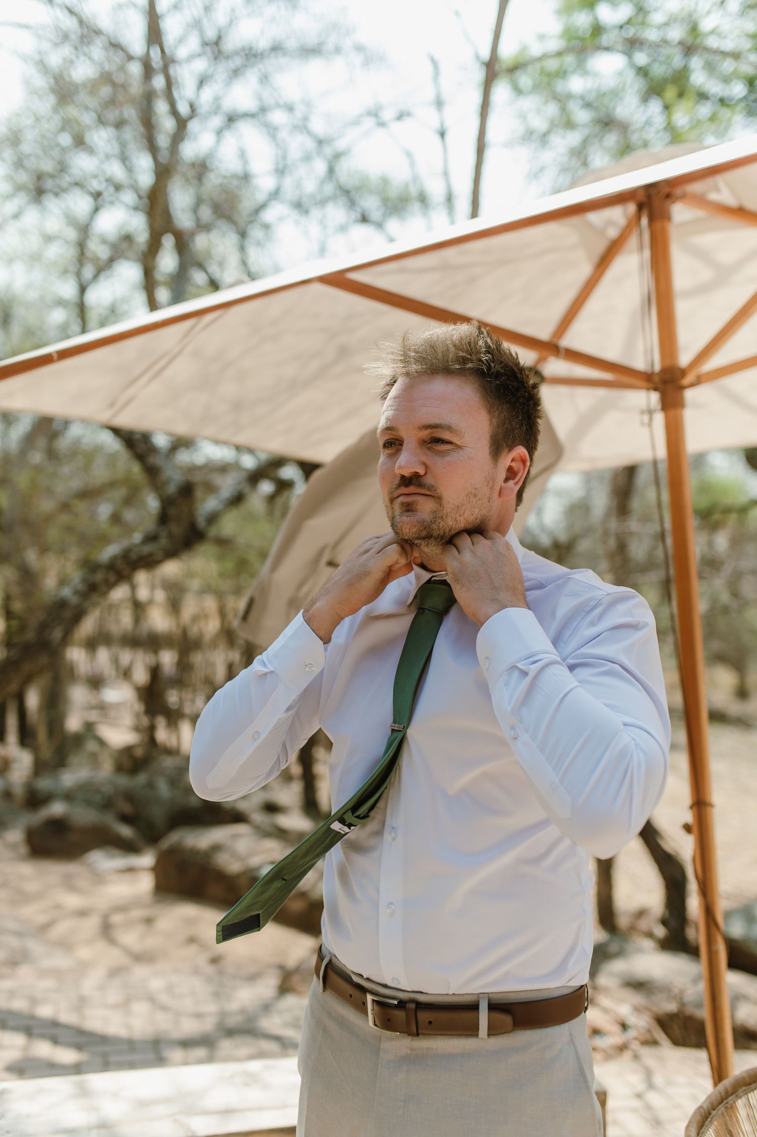 Person in white shirt adjusting tie in outdoor setting with umbrellas.