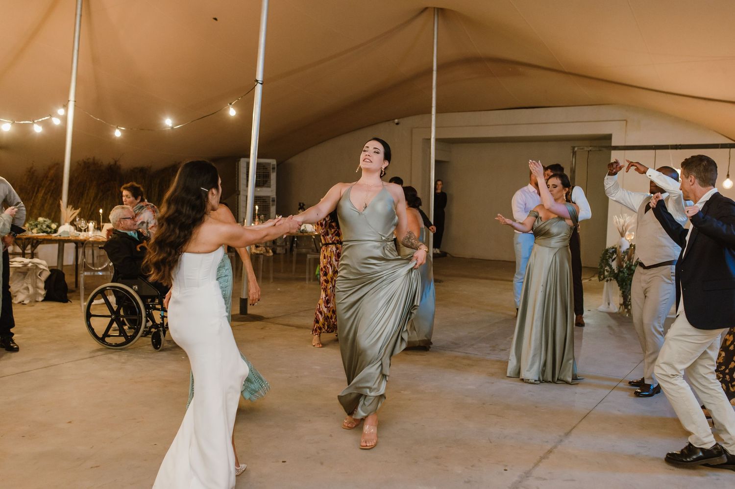 Wedding reception dance floor filled with guests celebrating under string lights.