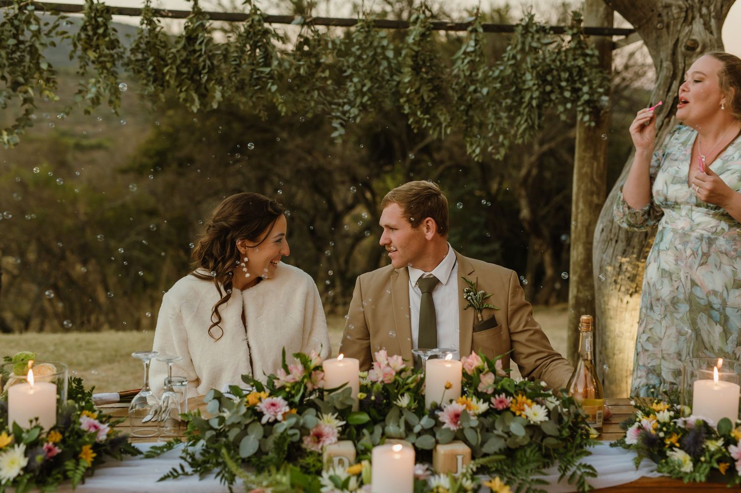 Garden wedding reception setup with floral arrangements and natural greenery overhead.