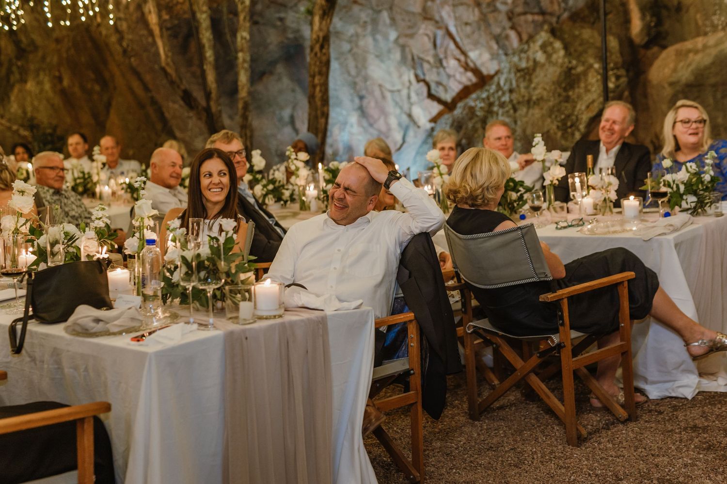 Rustic outdoor wedding reception with white tablecloths and hanging fairy lights creating ambiance.