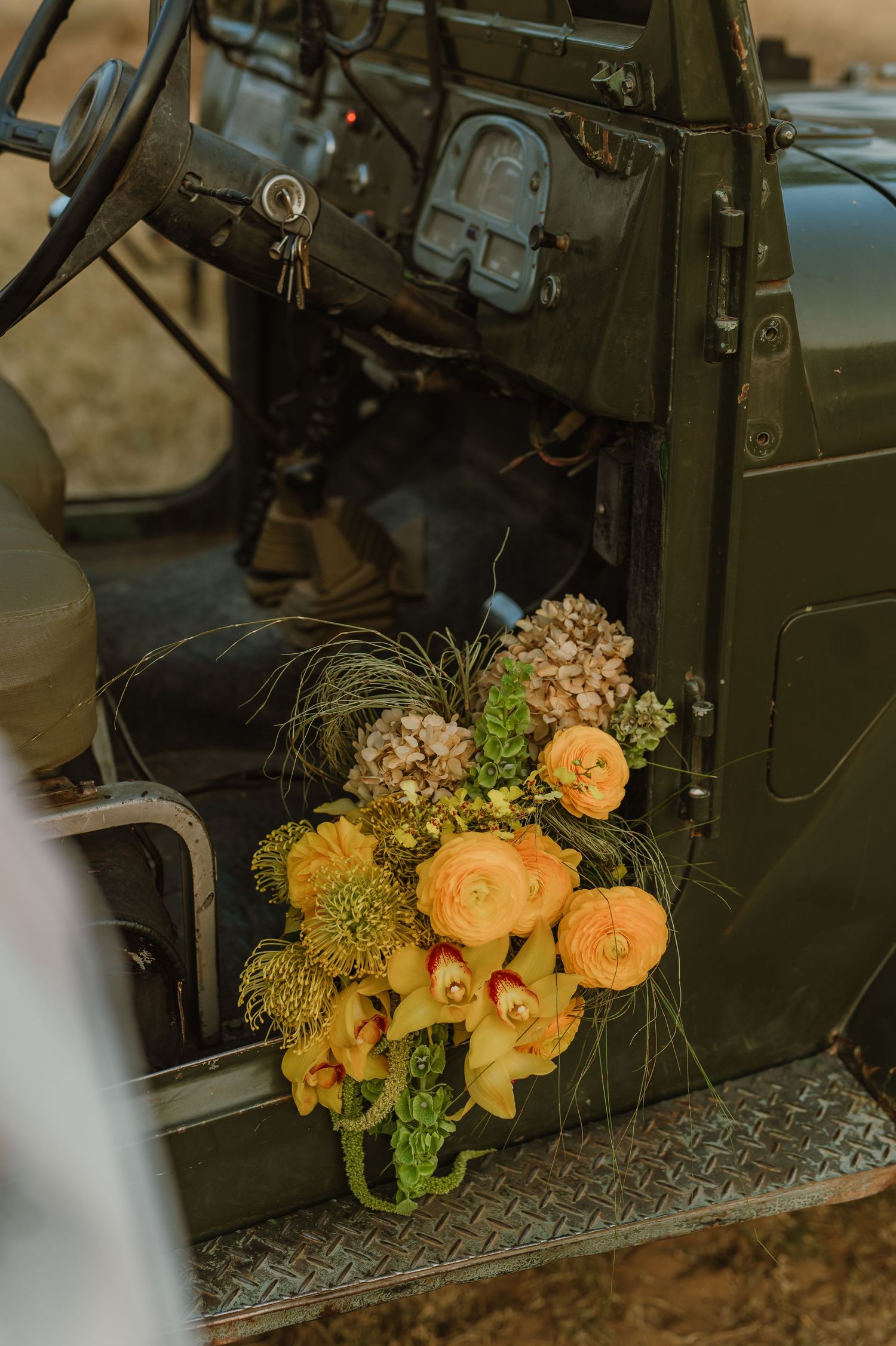 Yellow and peach floral bouquet arrangement displayed on vintage military vehicle.