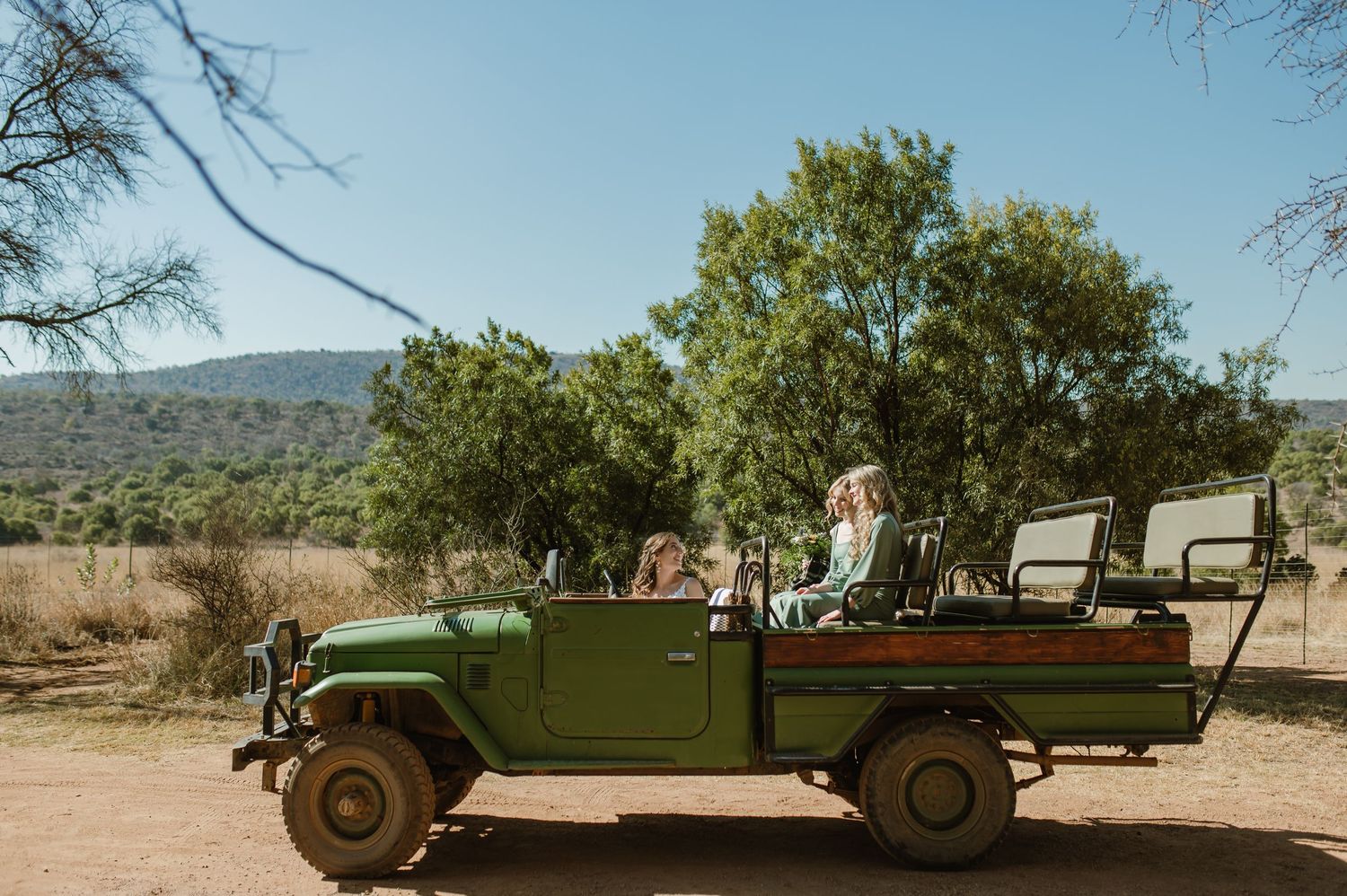 An open-air safari vehicle traverses through arid terrain with mountains in the background.