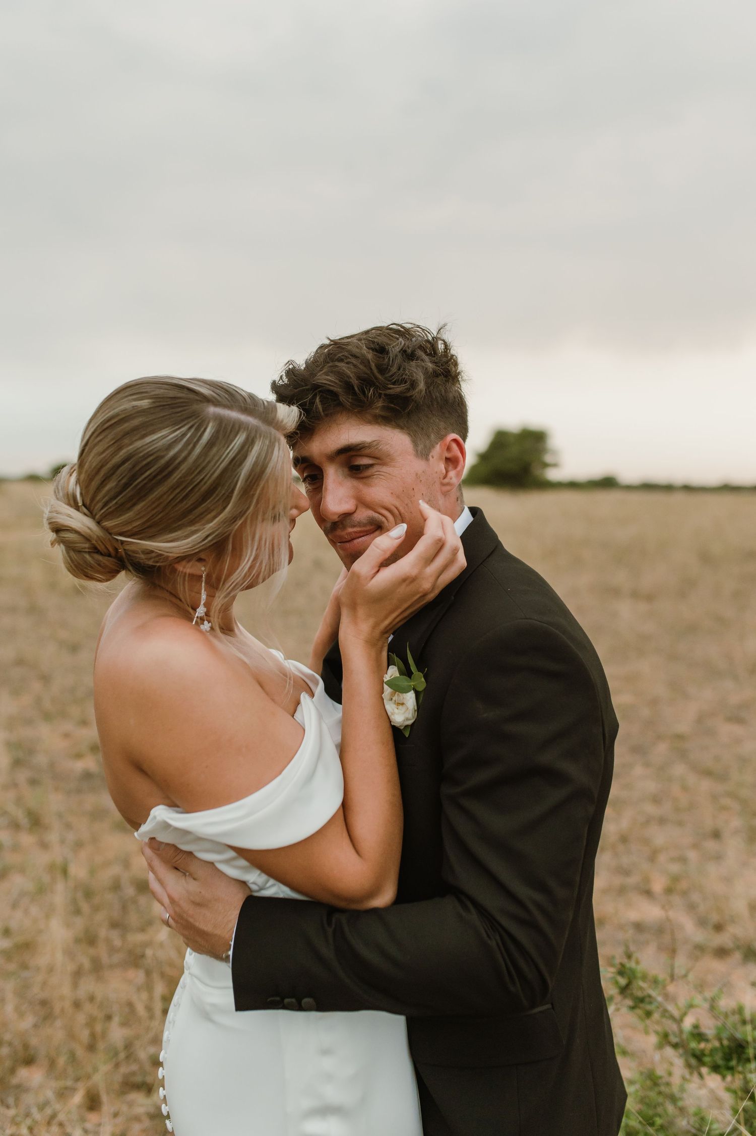 Couple embraces tenderly in an outdoor wedding photoshoot against a natural landscape.