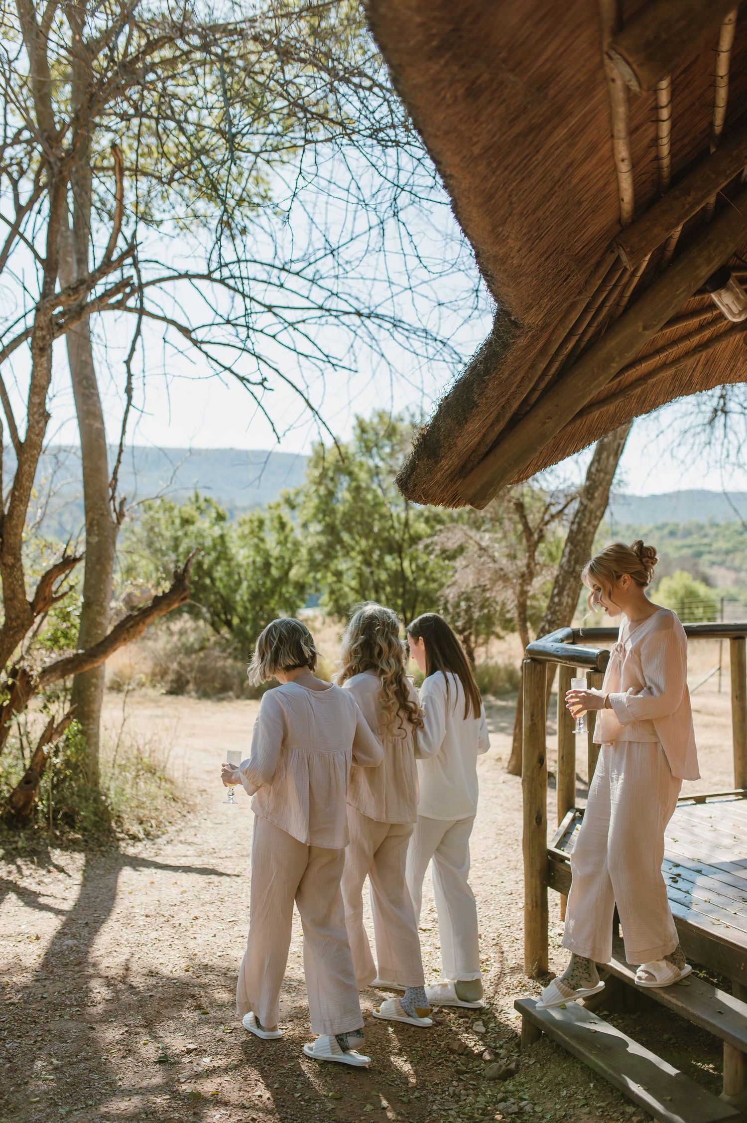 Group wearing all white outfits walking together in a desert landscape with trees and mountains in background.