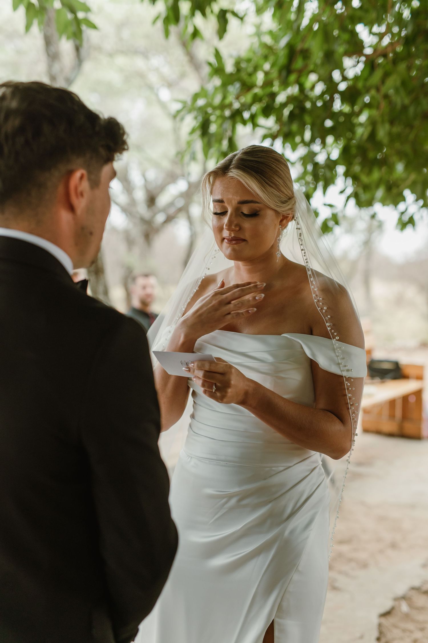 Emotional wedding ceremony moment captured in a natural outdoor setting with leafy green backdrop.