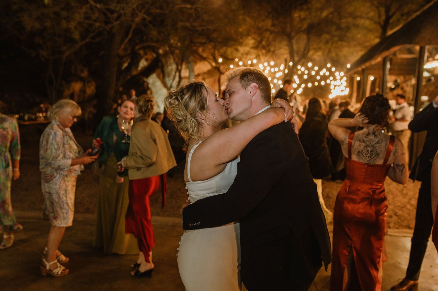 Wedding guests dancing and celebrating on a rustic dance floor under warm lighting and string lights.