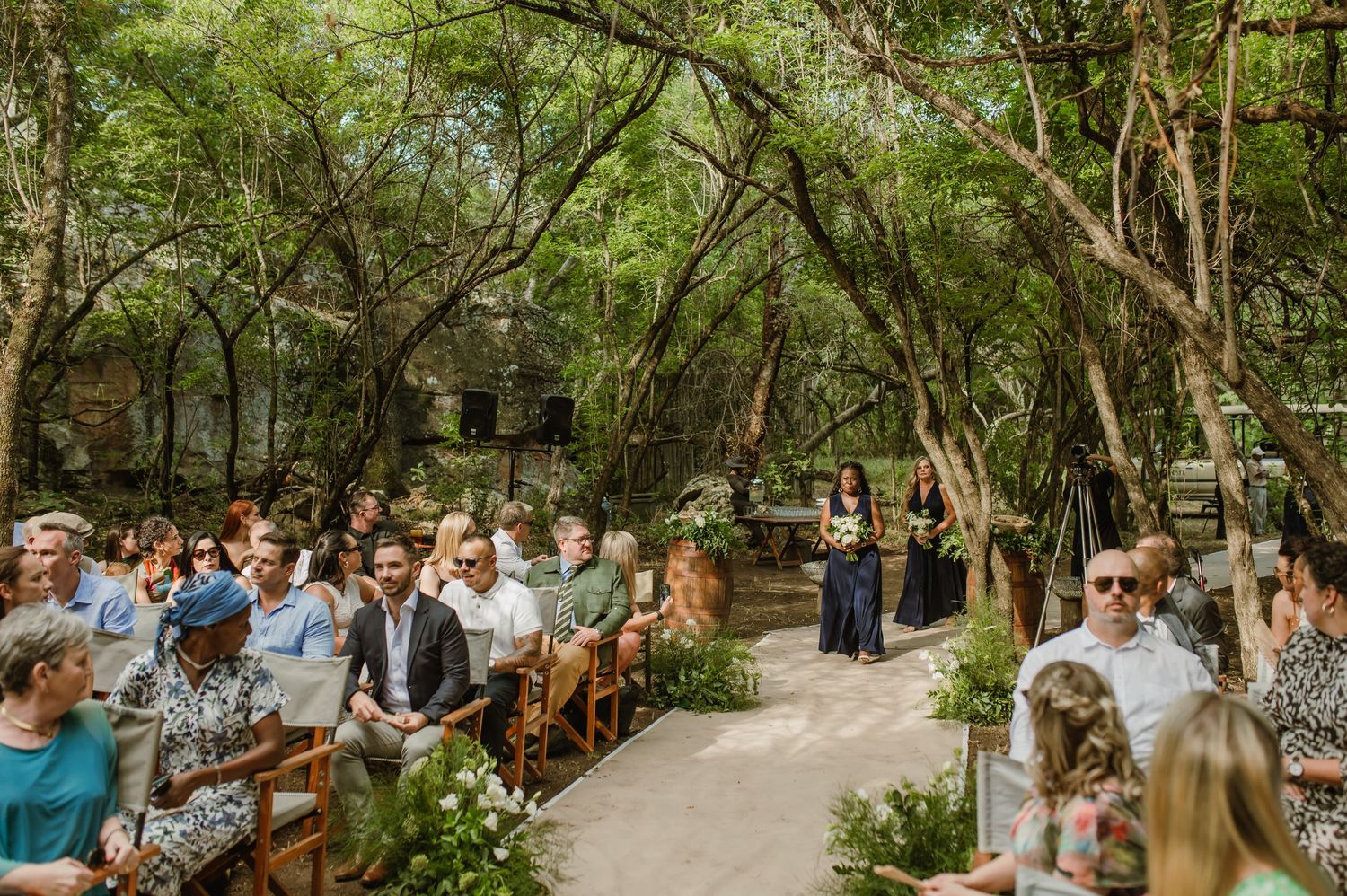 Sunlit forest wedding ceremony with guests seated along a natural pathway.