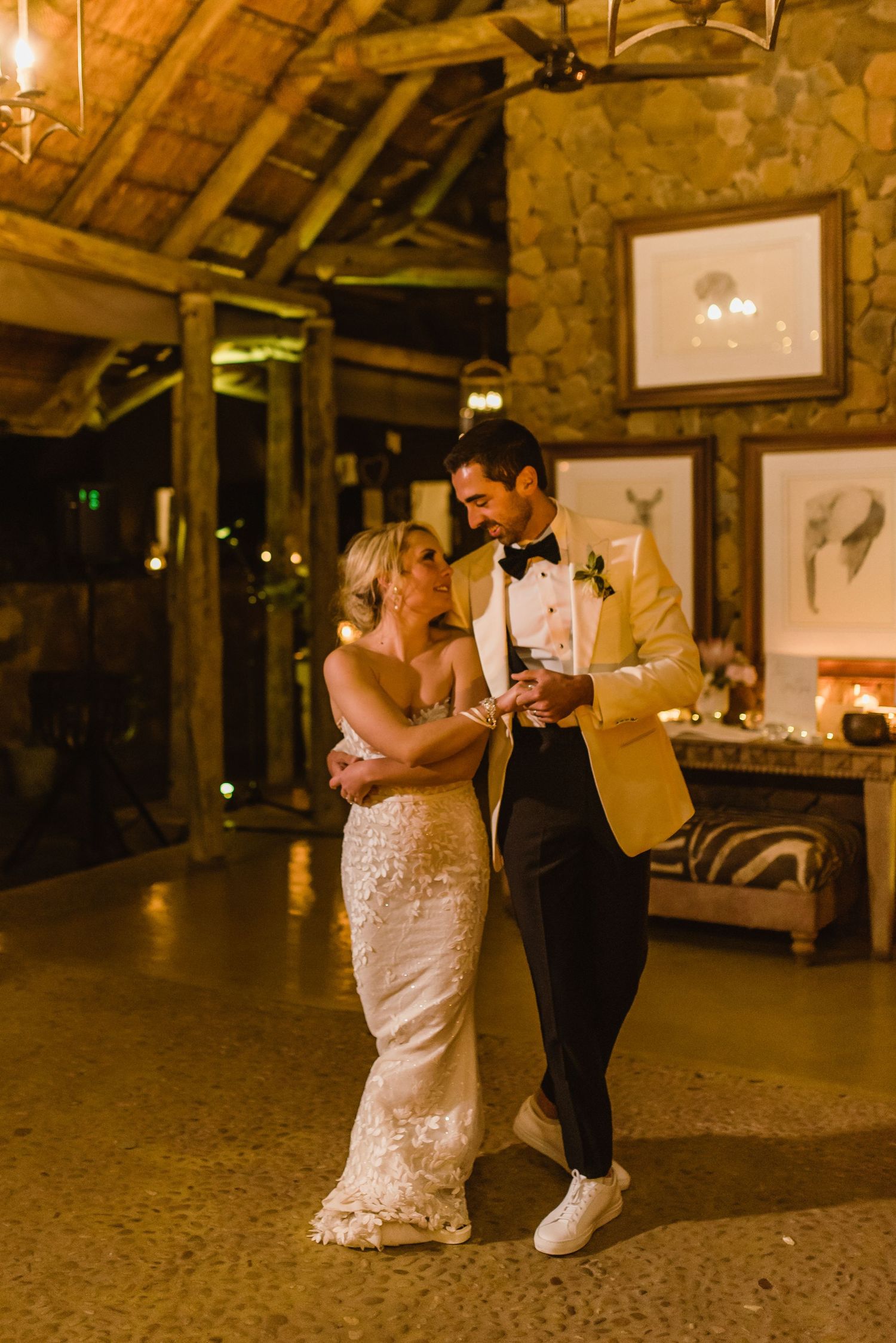 Wedding couple dancing in a rustic barn setting with string lights and wooden beams overhead.