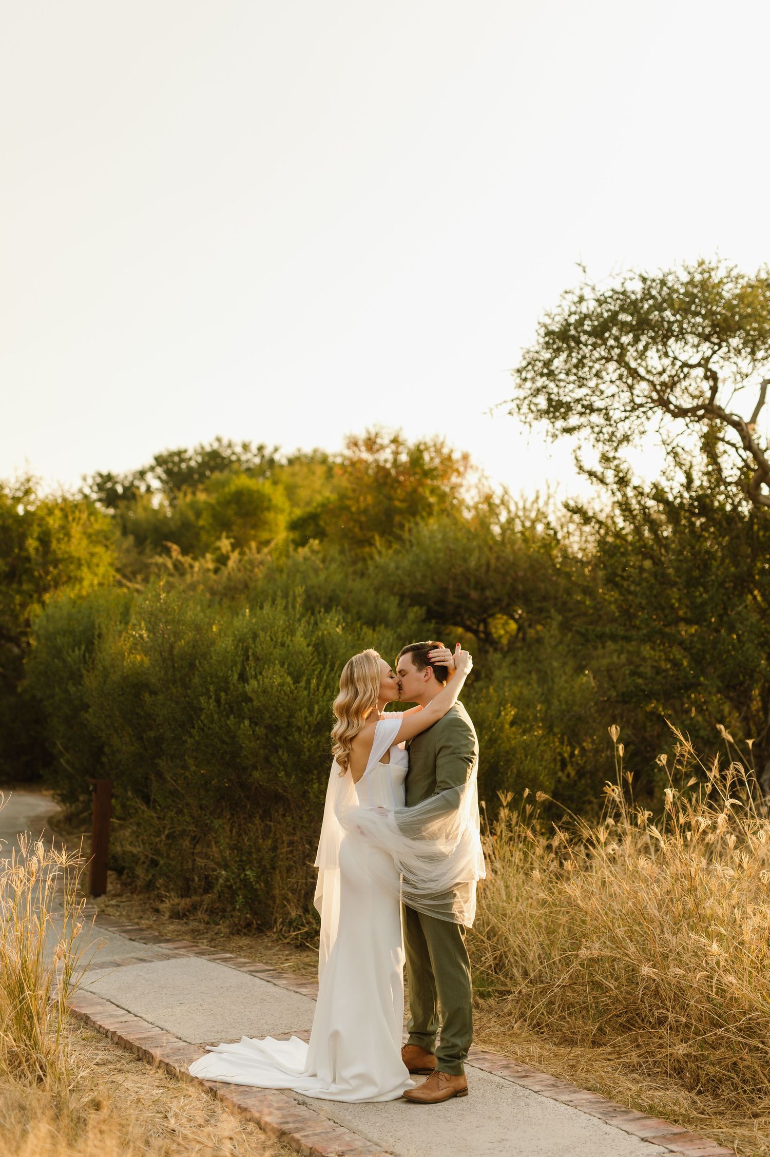 Romantic wedding portrait of a couple embracing on a nature trail during sunset.