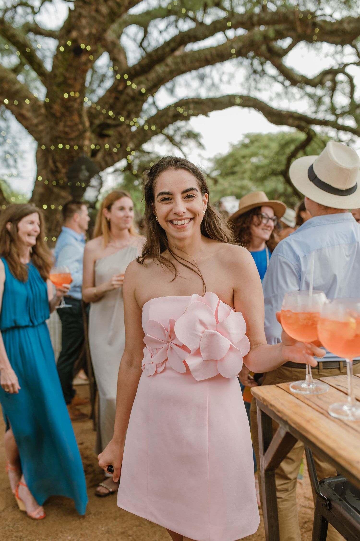 Outdoor party setting with string lights and guests mingling under trees.