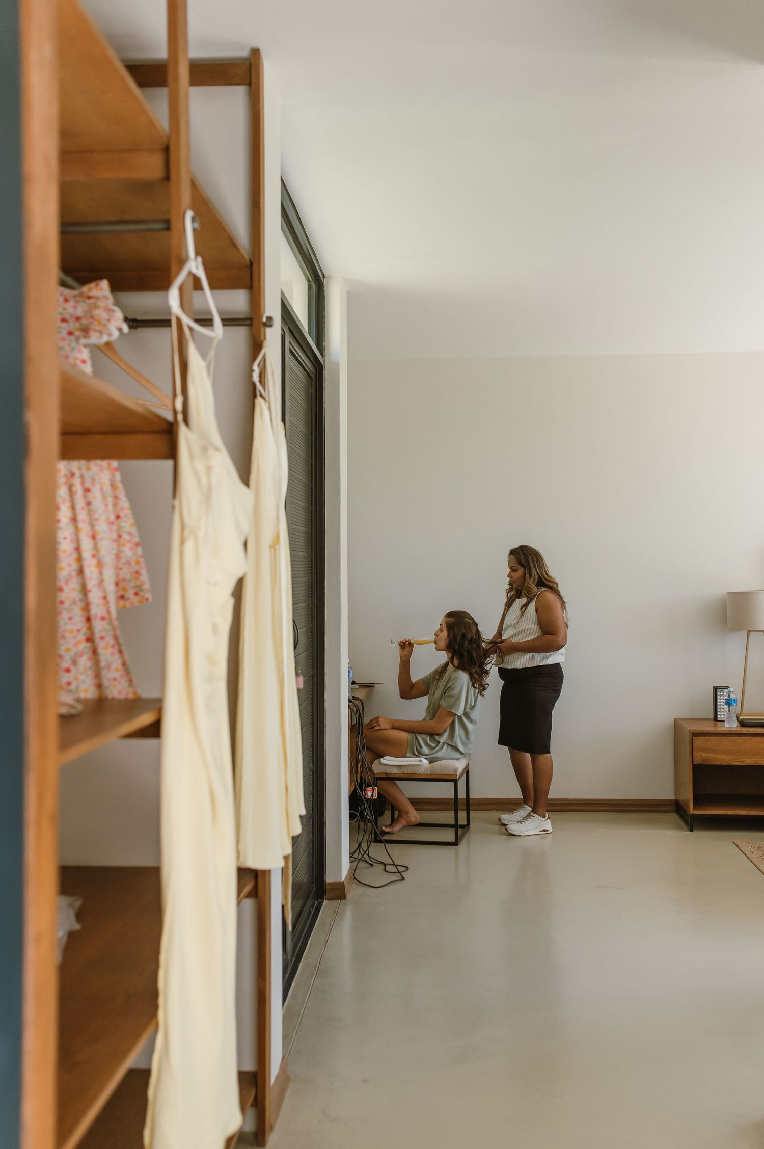 White wedding dress hangs in minimalist room with natural lighting.