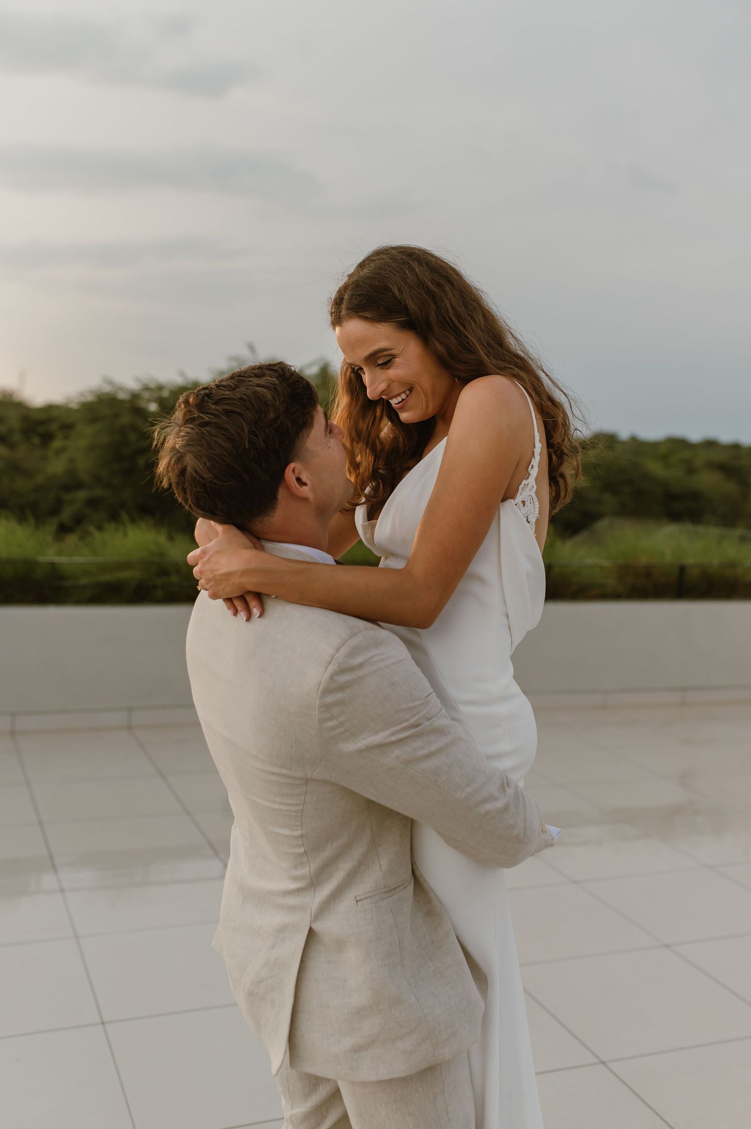 A romantic wedding couple embraces on a white tiled terrace during golden hour.