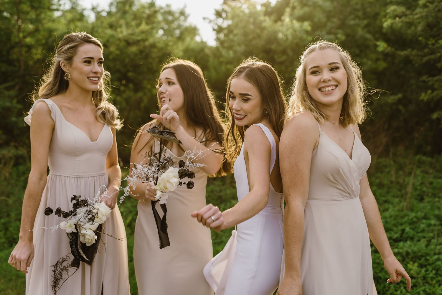 Bridesmaids in pastel dresses holding bouquets and smiling outdoors.