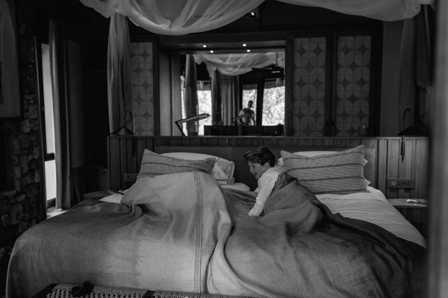 Black and white photo of a person resting on a bed in an elegantly decorated bedroom.
