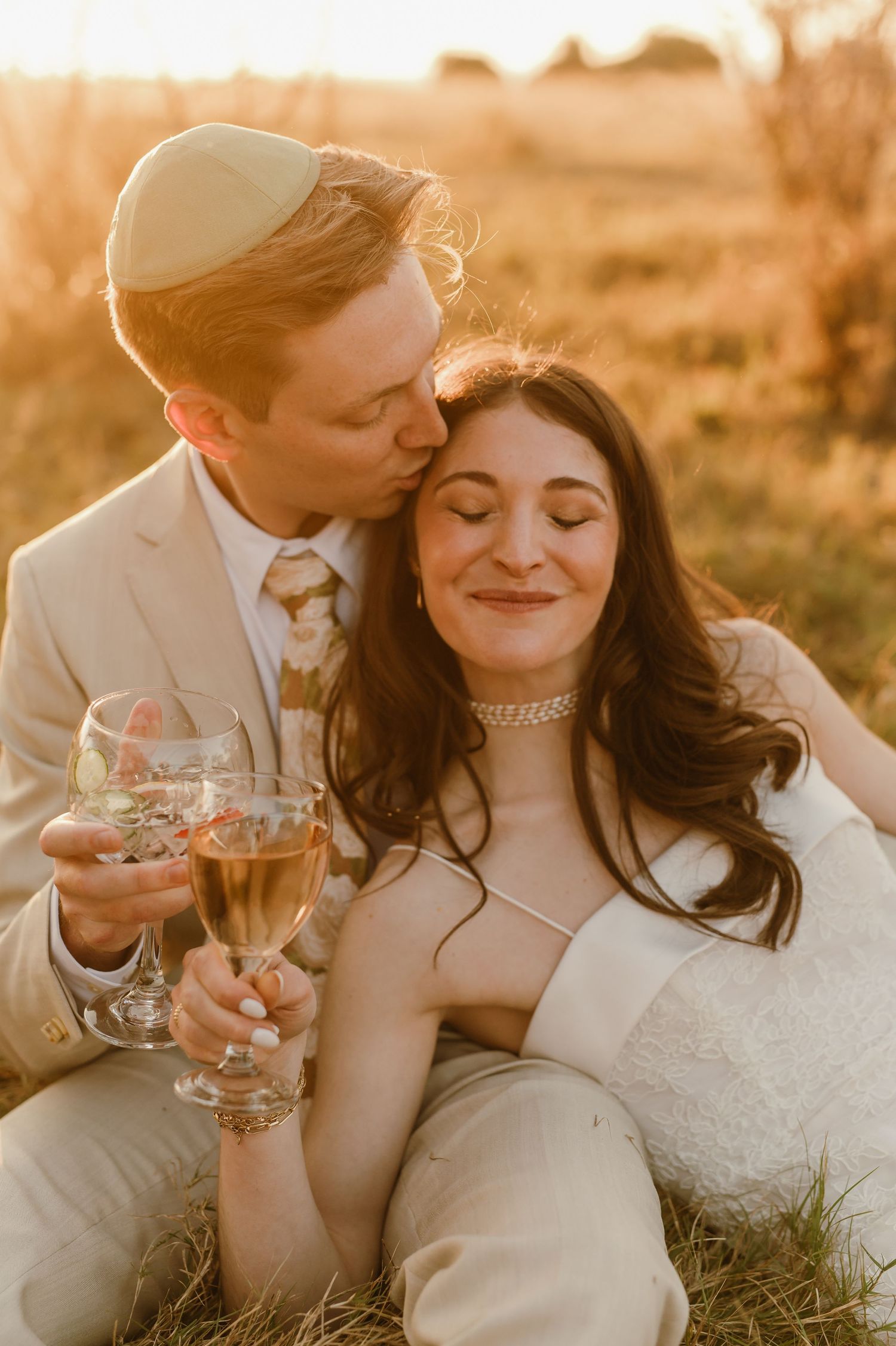 Bride and groom sharing a romantic sunset moment with champagne glasses in a golden field.
