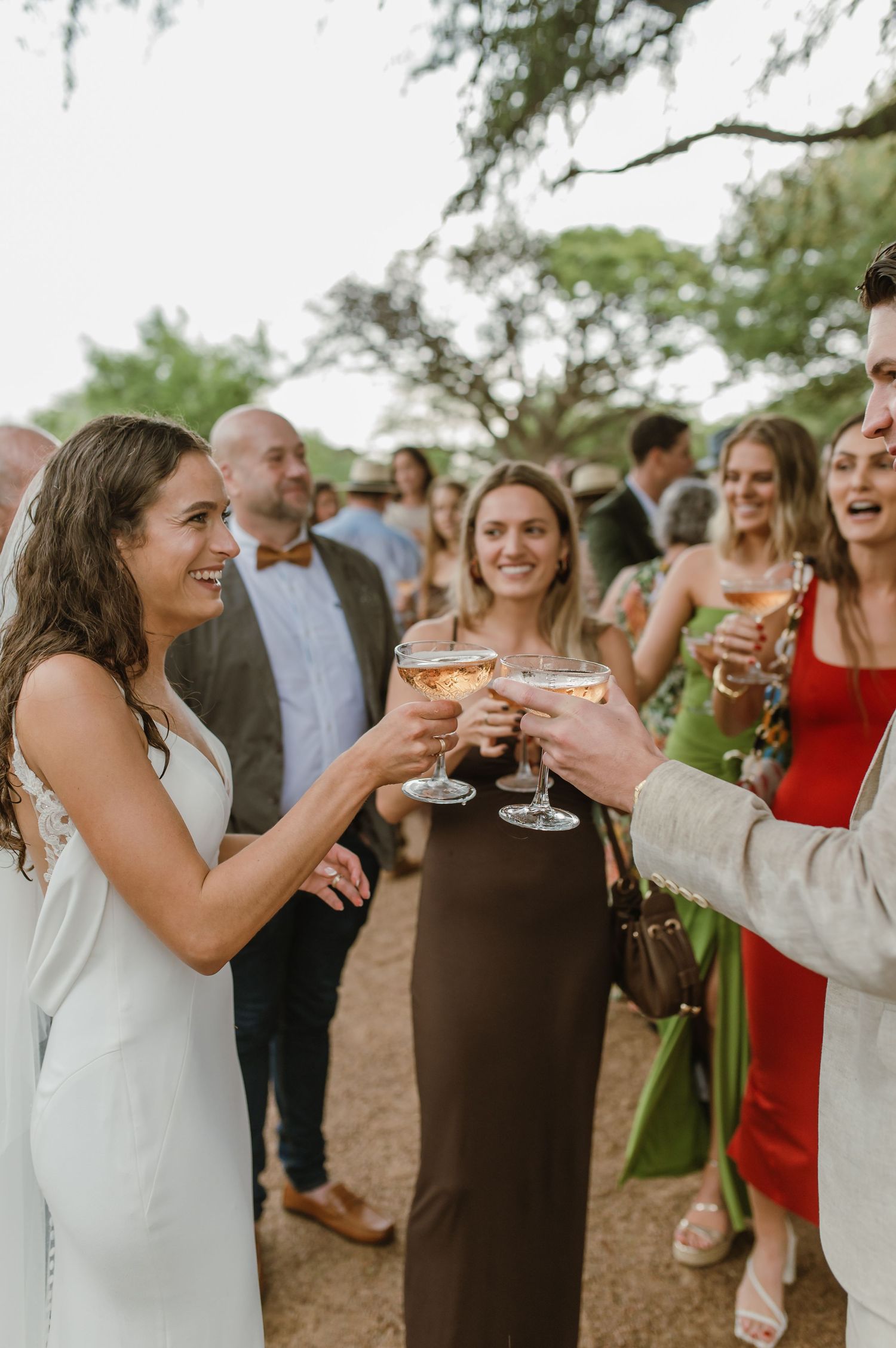 Festive group of wedding guests sharing drinks and laughter at outdoor reception.