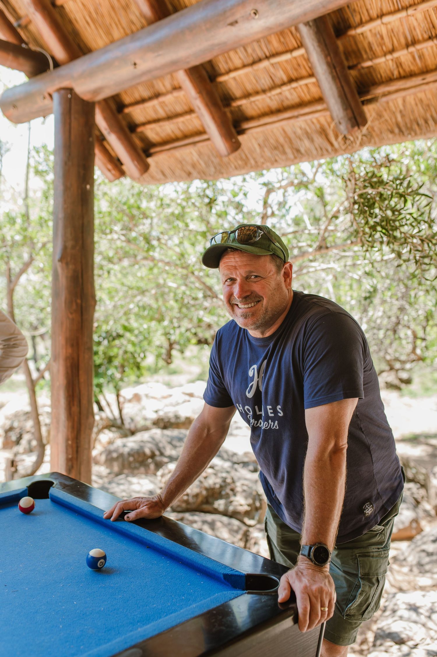 Someone playing pool under a rustic wooden pavilion with natural lighting.