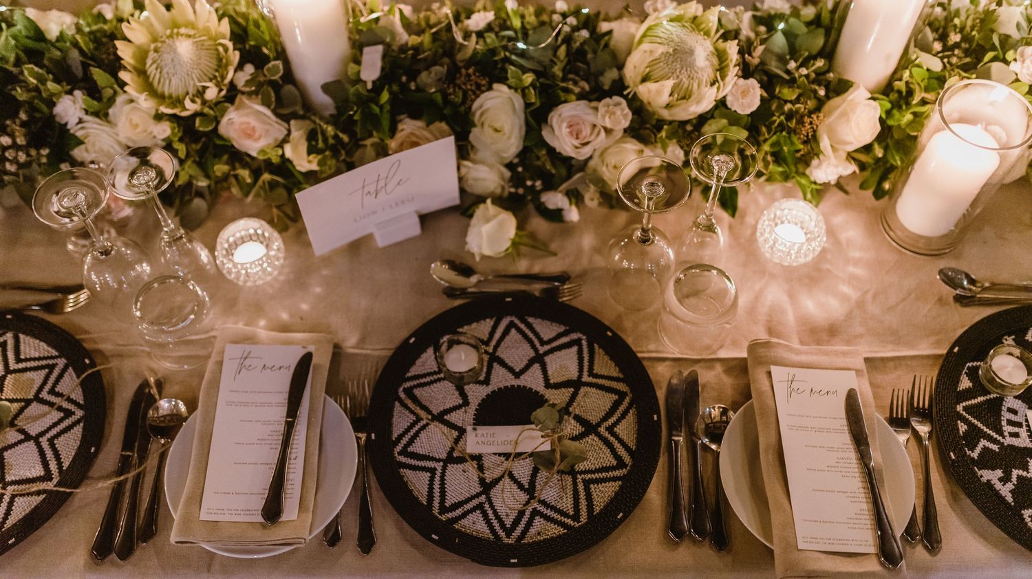 Overhead view of elegant table settings with black chargers and white floral centerpieces.