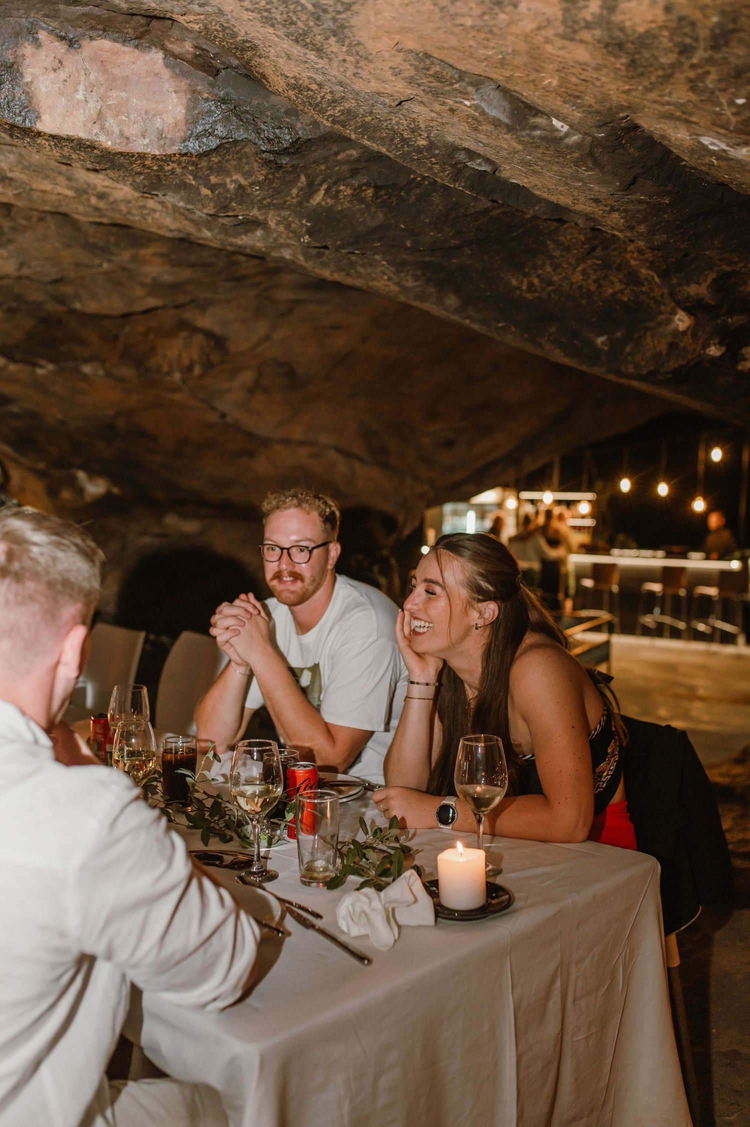Diners enjoying conversation at a candlelit table in a cave restaurant setting.