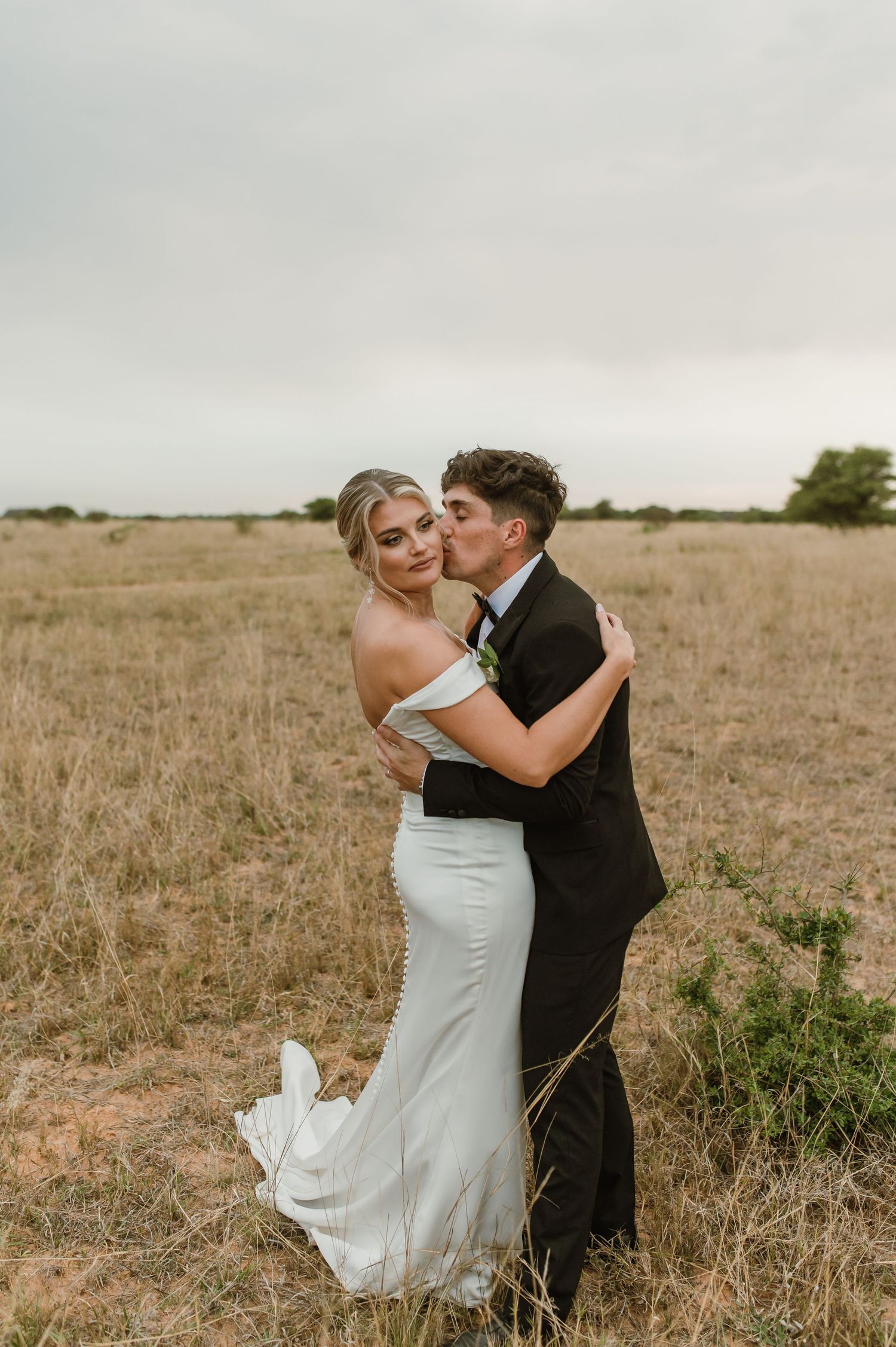 Newlyweds share an intimate moment in a rustic field during golden hour.