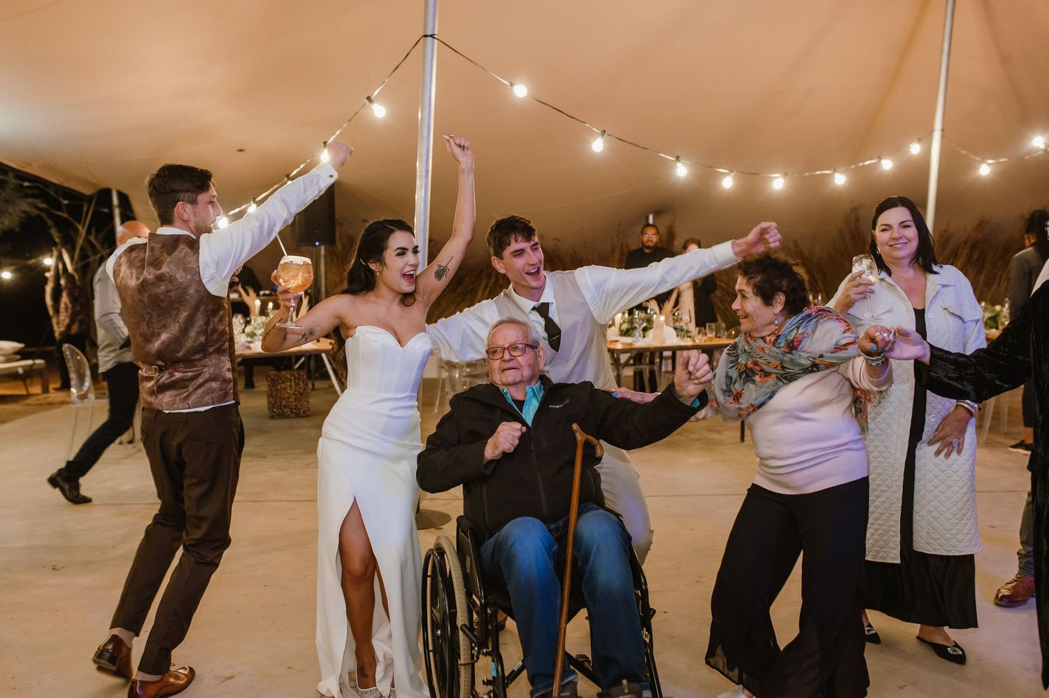 Guests enjoying lively dancing and celebration at an outdoor tented wedding reception.