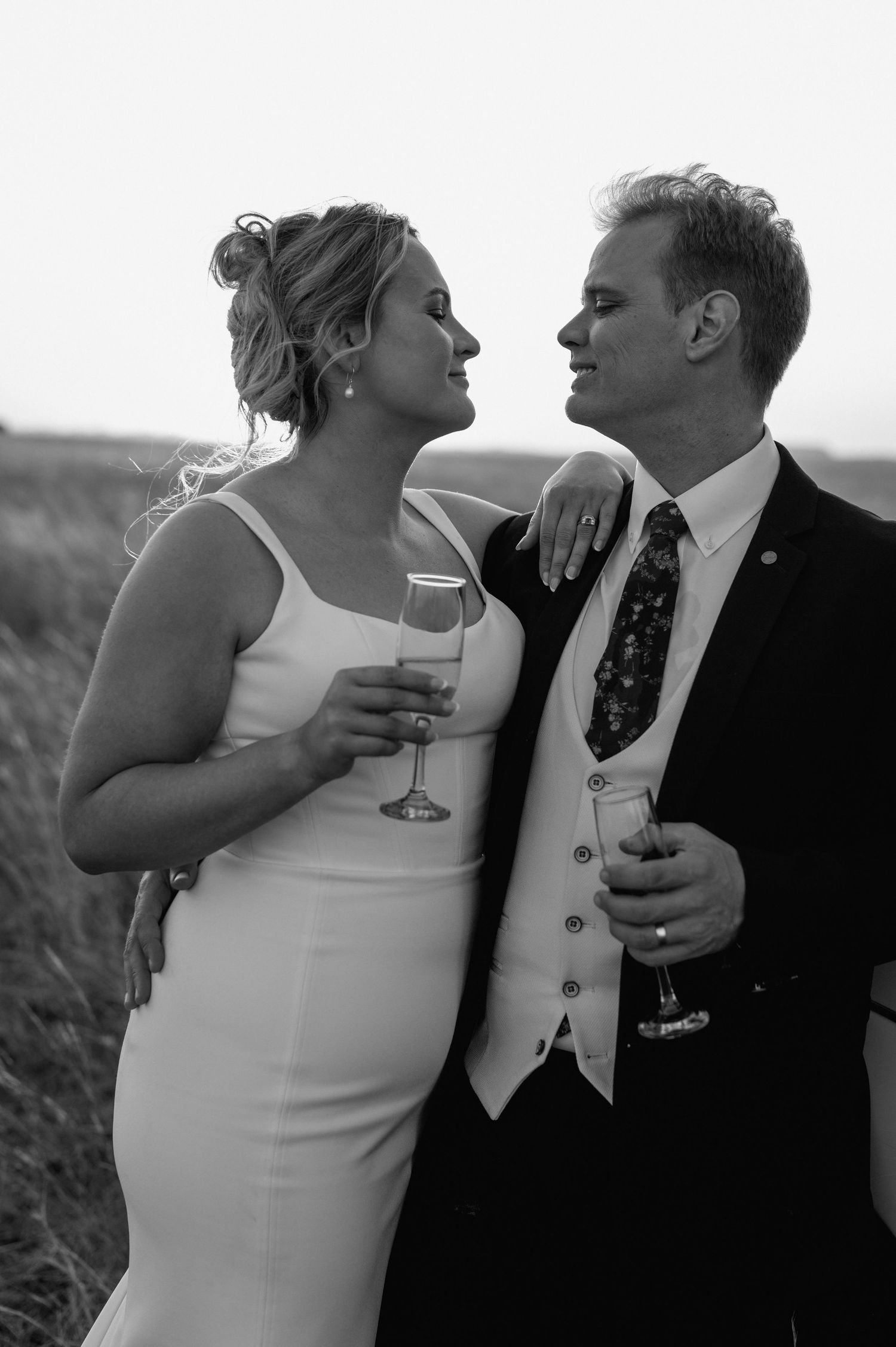 Black and white portrait of couple sharing champagne during sunset wedding shoot.