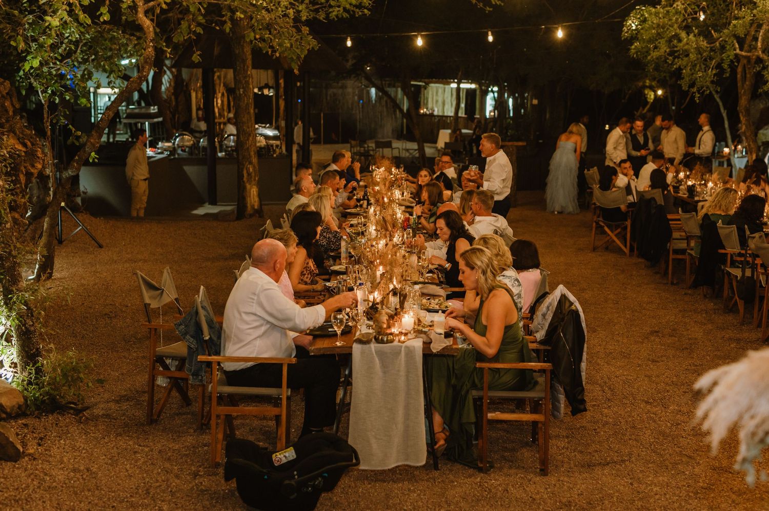 Guests enjoying dinner at long wooden tables during an outdoor evening wedding reception.