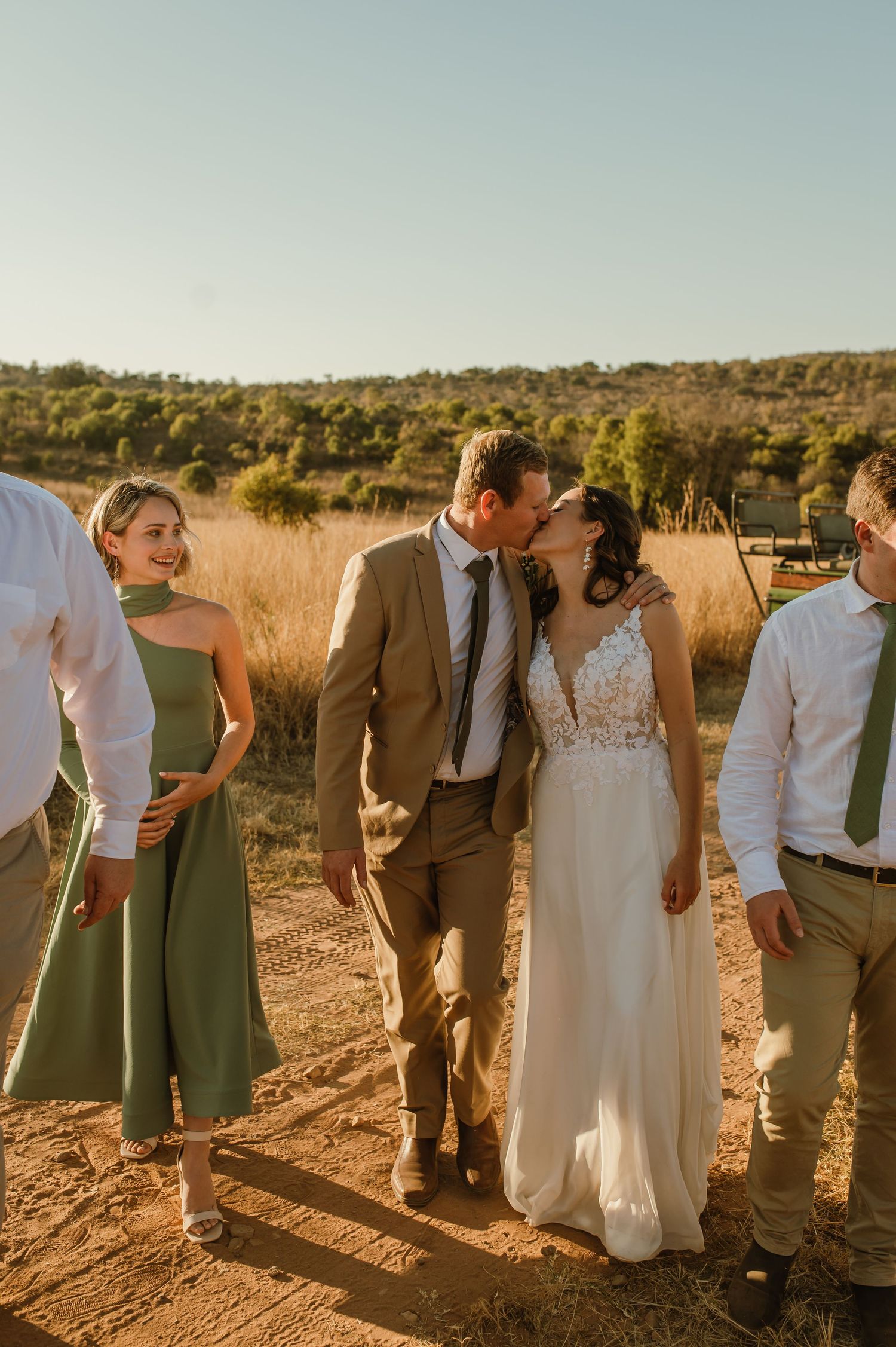 Wedding party walks together through a golden field at sunset wearing sage green and neutral attire.