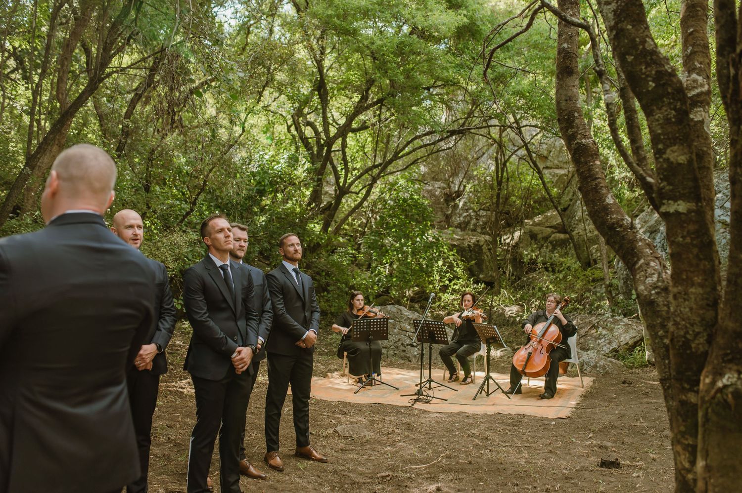Outdoor wedding ceremony in a lush forest setting with guests gathered on wooden chairs.