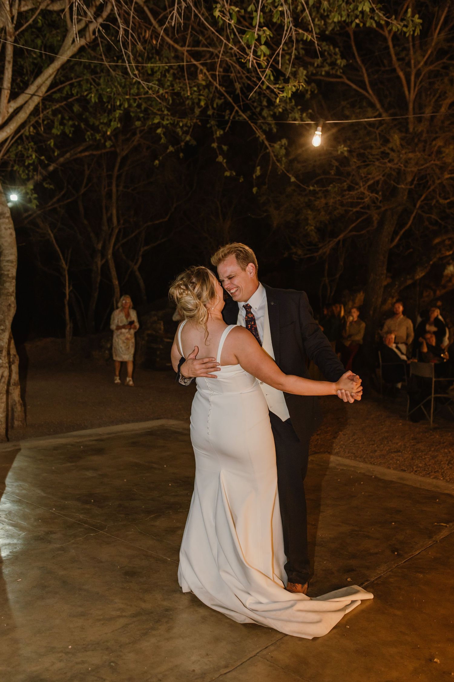Wedding dance celebration on an outdoor patio beneath string lights and trees.